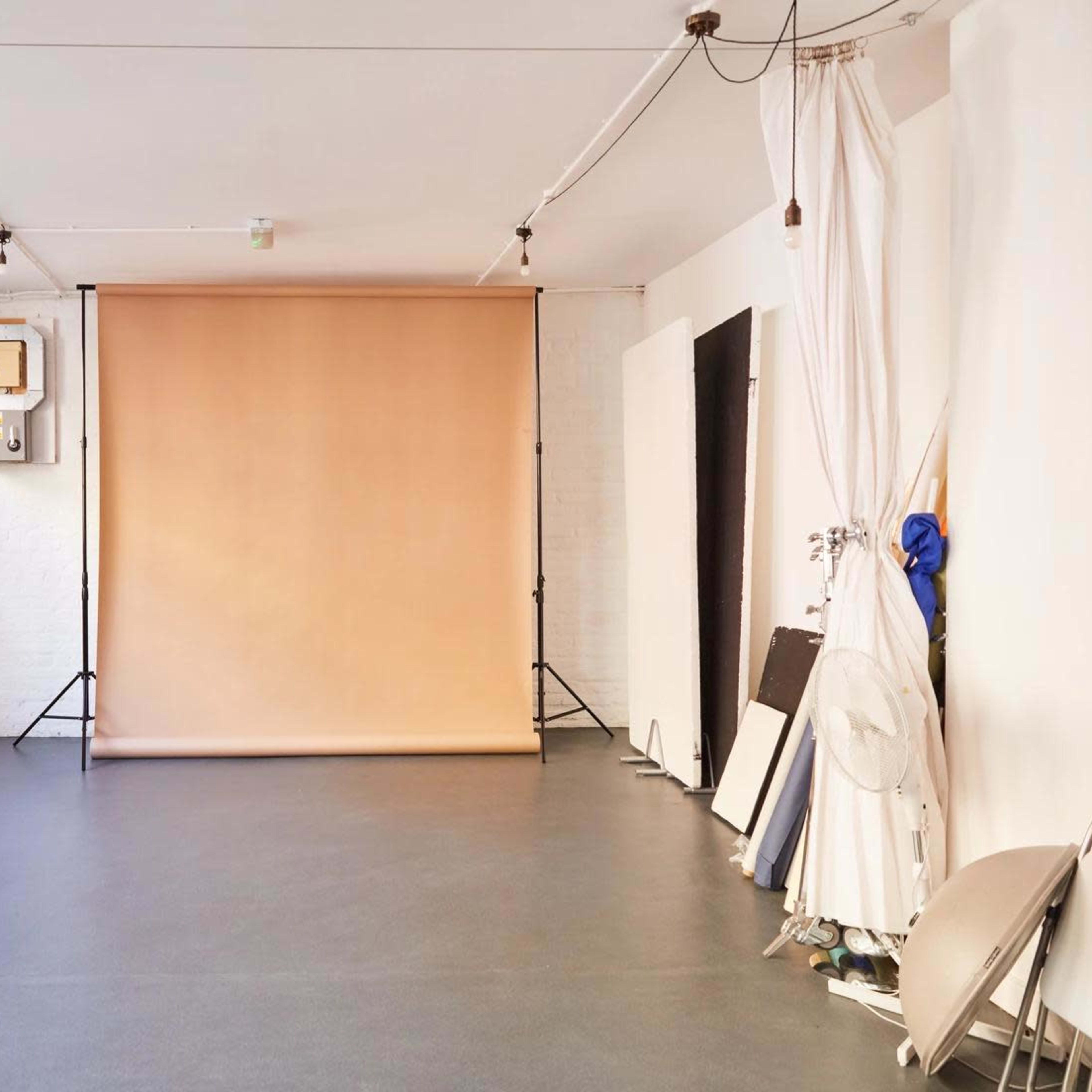 A spacious, empty studio with a beige backdrop, a desk, and various photography equipment along the walls.