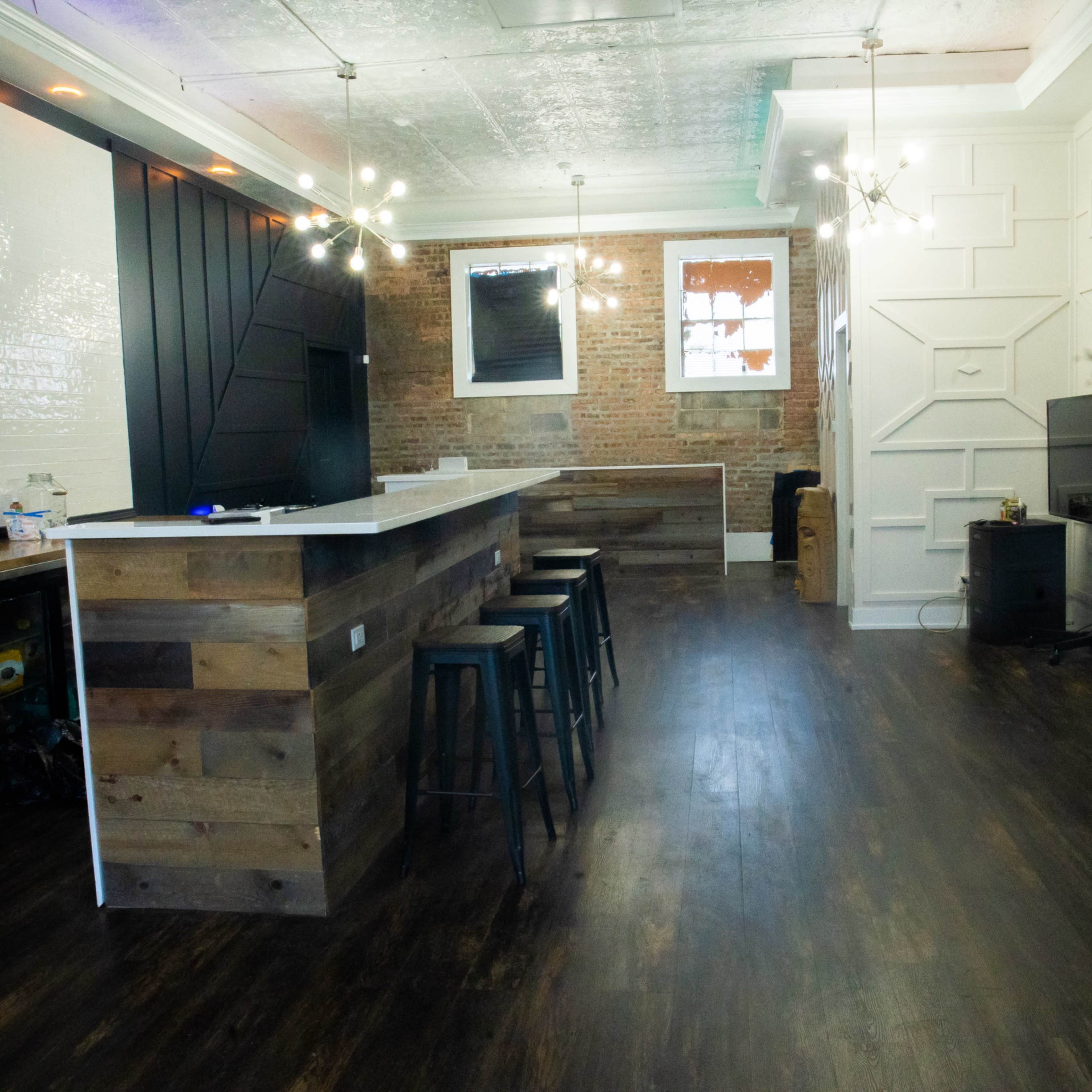 A spacious interior featuring an industrial-style kitchen with a wooden bar, metal stools, and exposed brick walls.