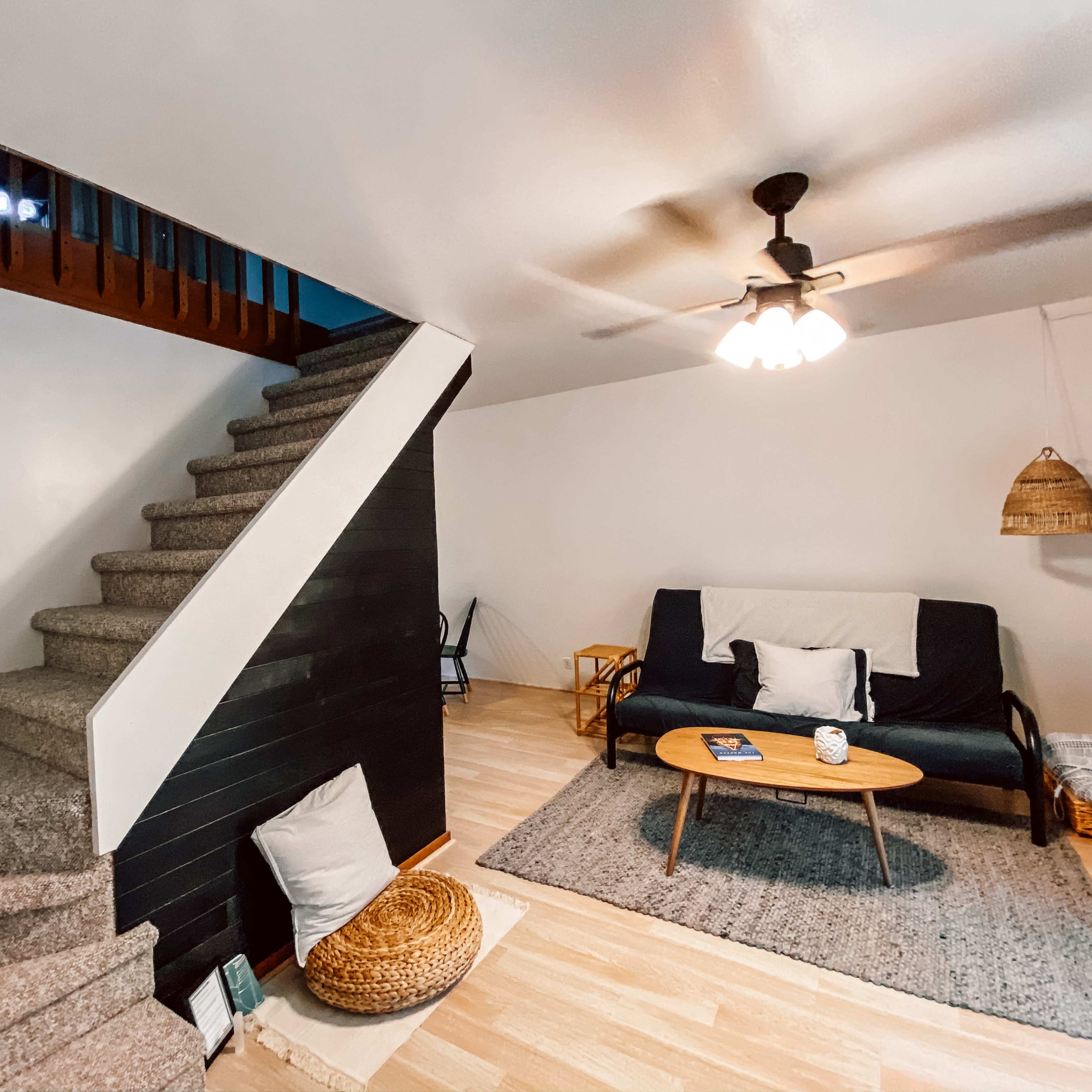 A living room with a staircase, a couch with pillows, a coffee table, and a rug on the floor.