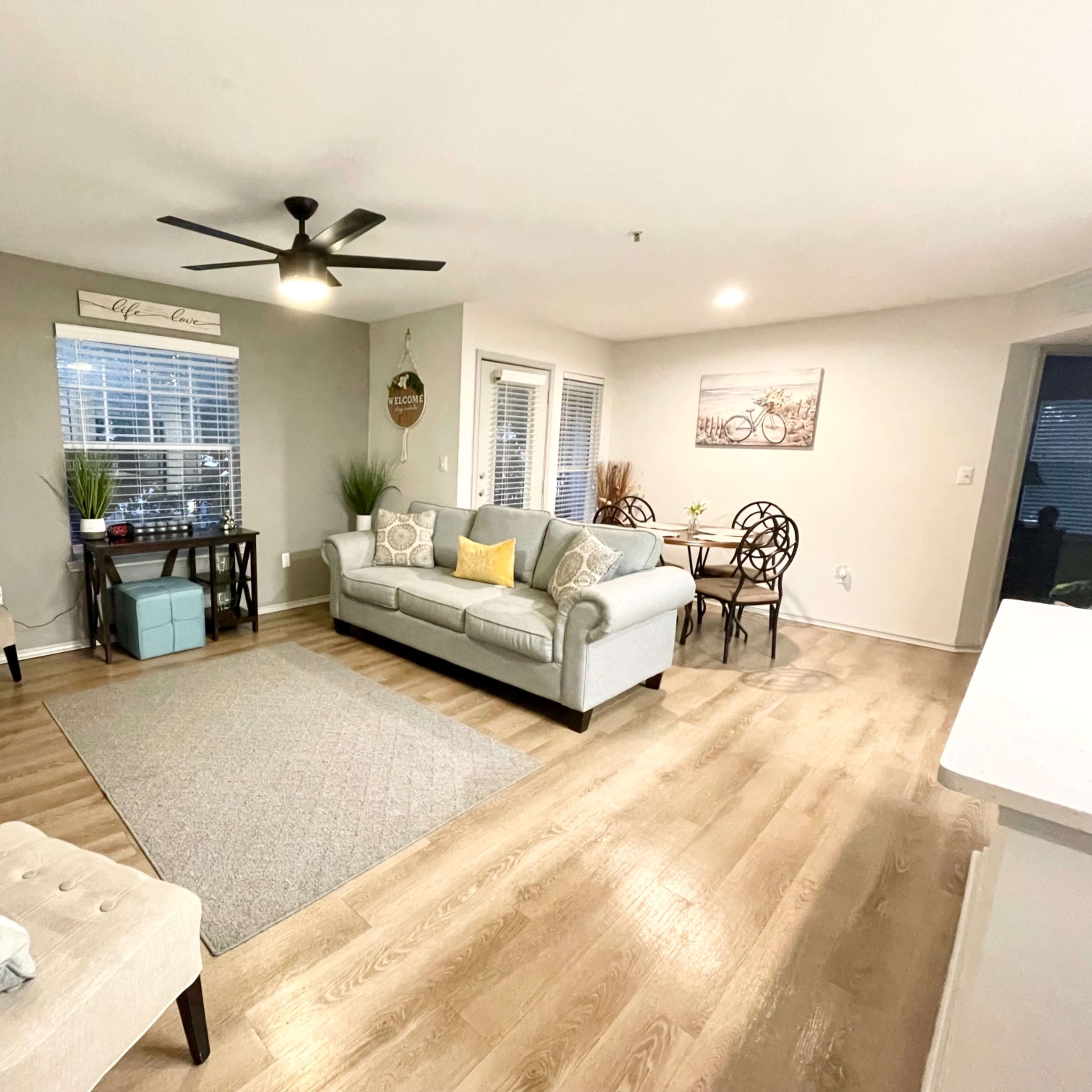 A modern living room with a sofa, armchair, coffee table, and a dining area, featuring a light color scheme and wooden flooring.