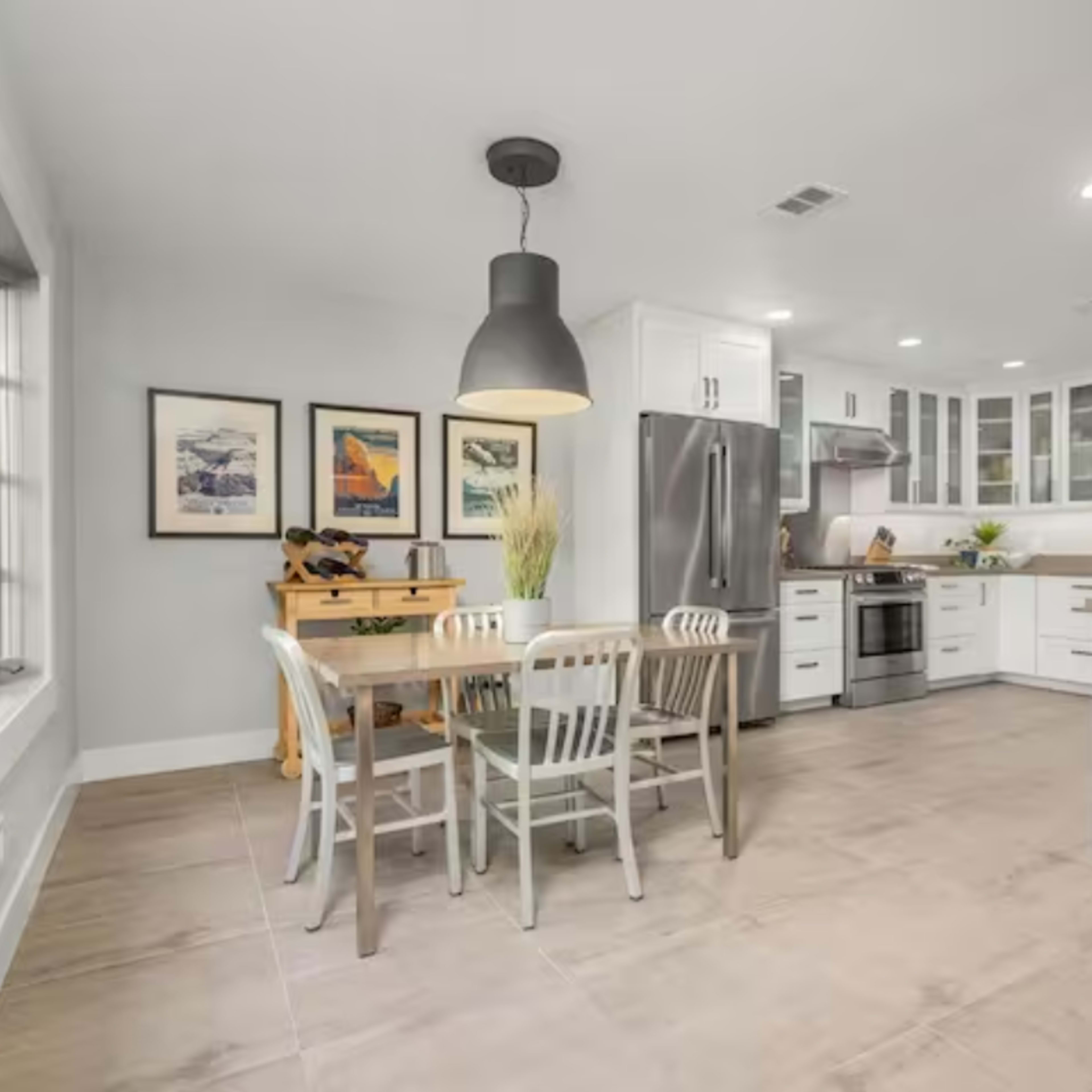 A modern kitchen features a dining table with four chairs, stainless steel appliances, and white cabinetry.