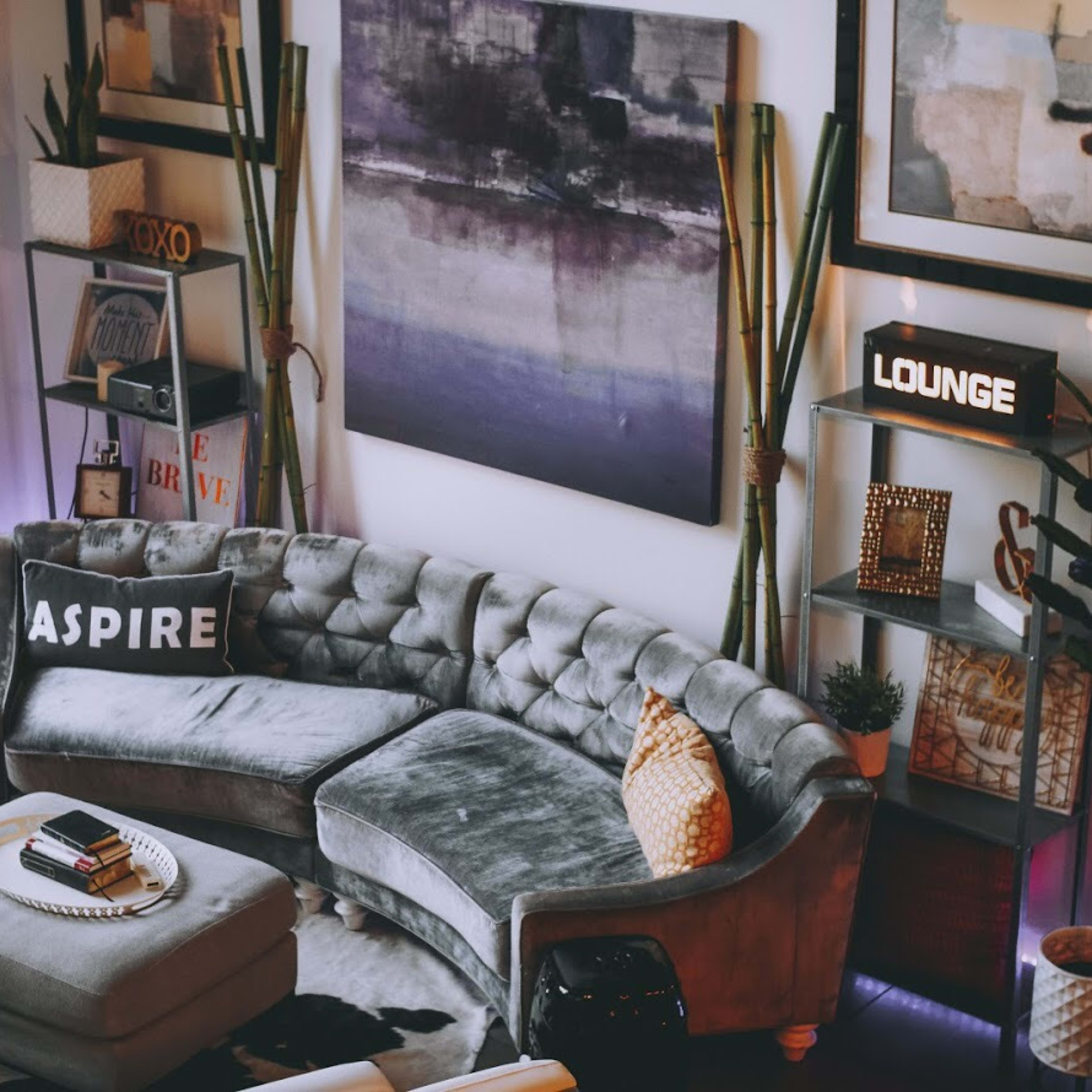 A modern living room with a gray sectional sofa, decorative cushions, a round coffee table, and wall shelves displaying various decor items.