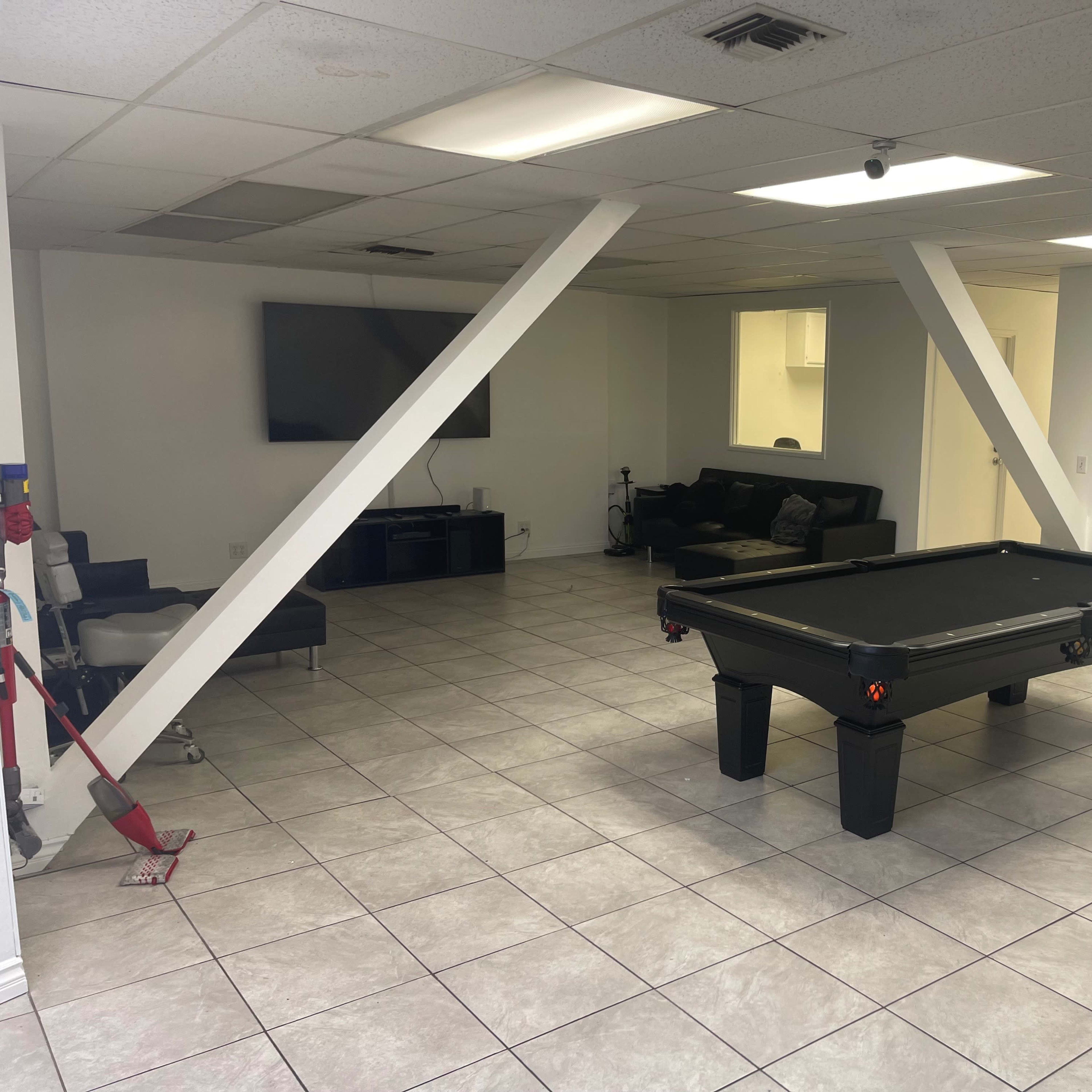 A spacious room with a pool table, a sectional sofa, a television mounted on the wall, and stark white walls.