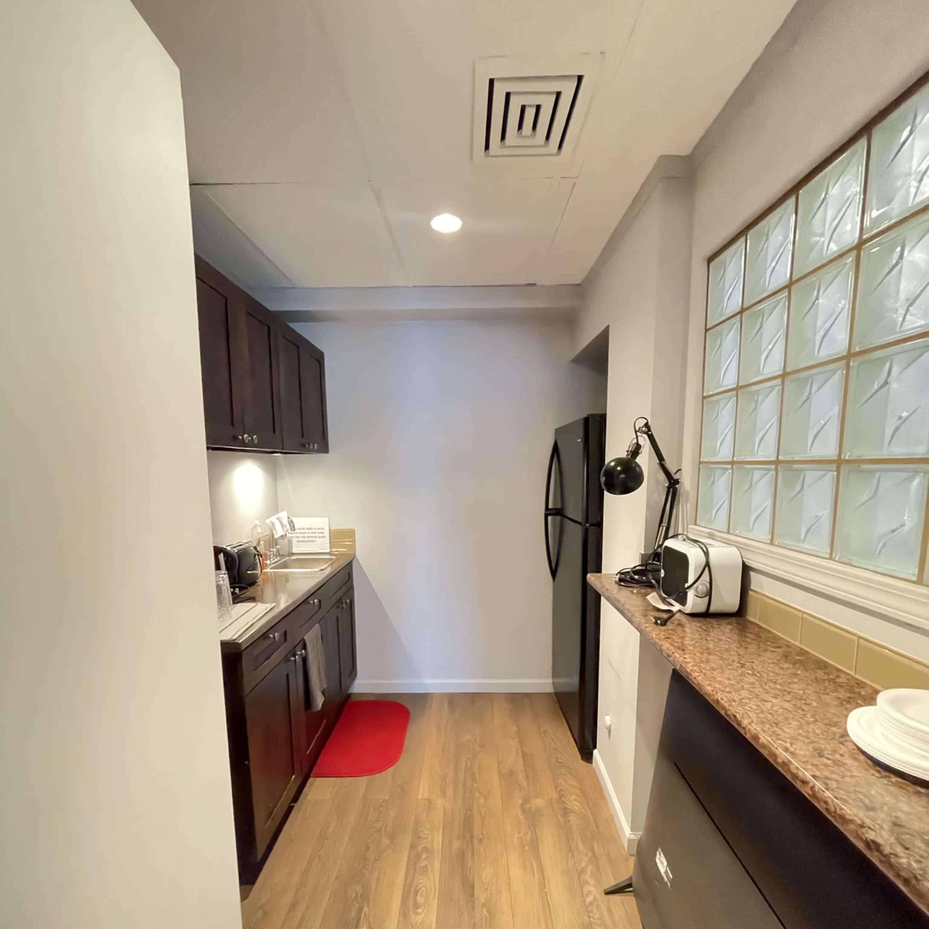 A narrow kitchen with dark cabinetry, a countertop, and modern appliances, featuring a red rug on the floor.