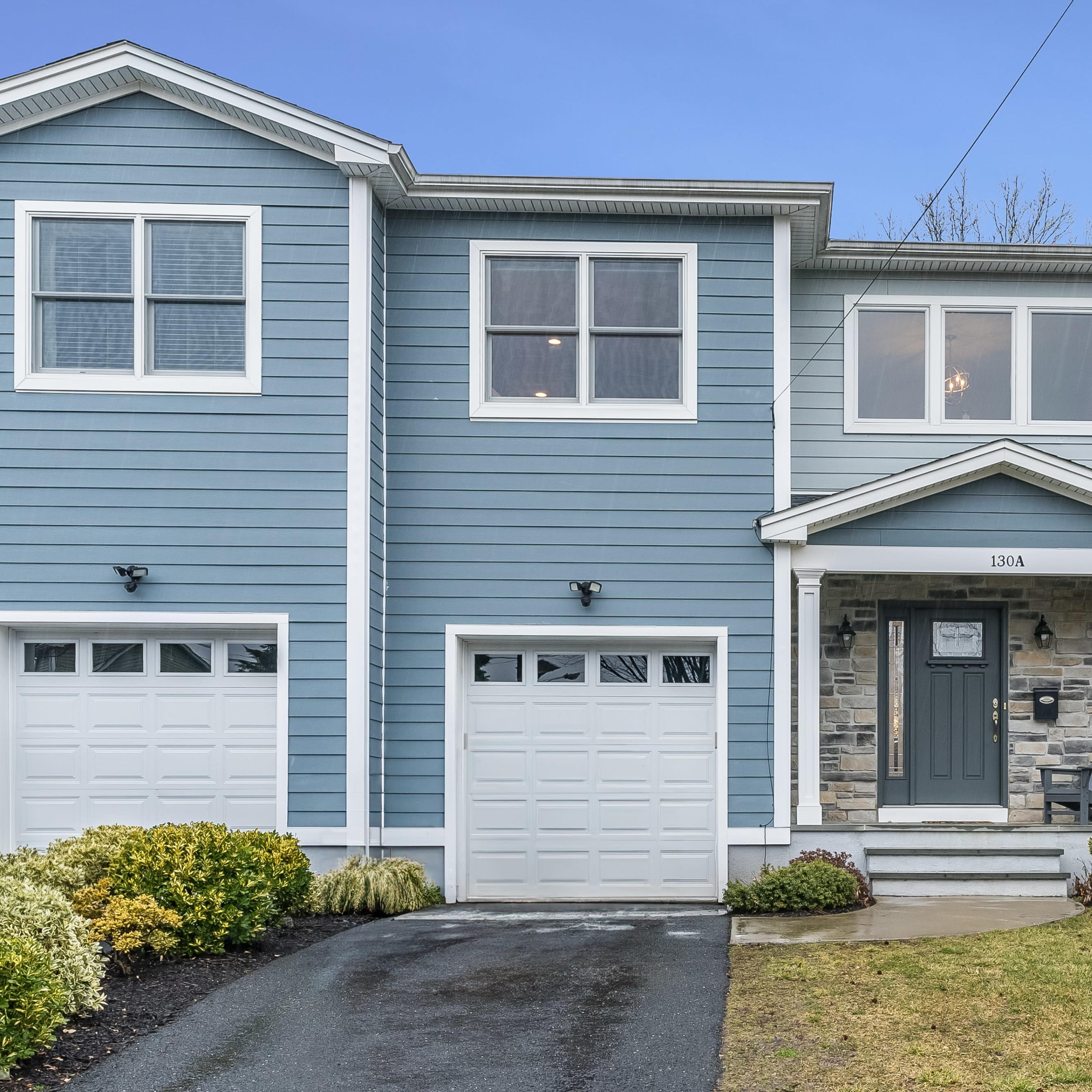 A blue, two-story townhouse with a stone-accented entrance, a driveway, and a garage on the left side.