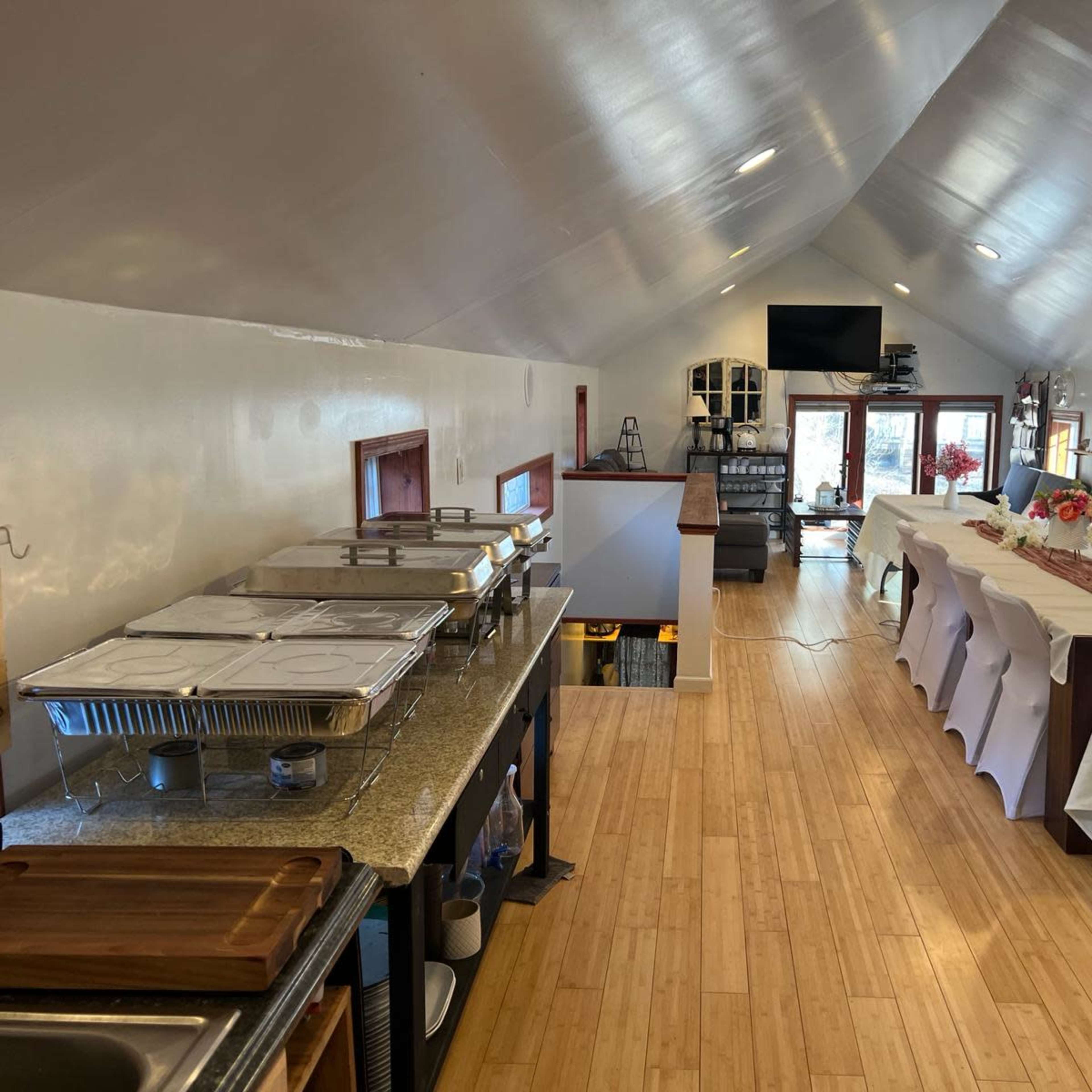 A spacious indoor venue with neatly arranged tables, catering trays on a counter, and a television screen mounted on the wall.