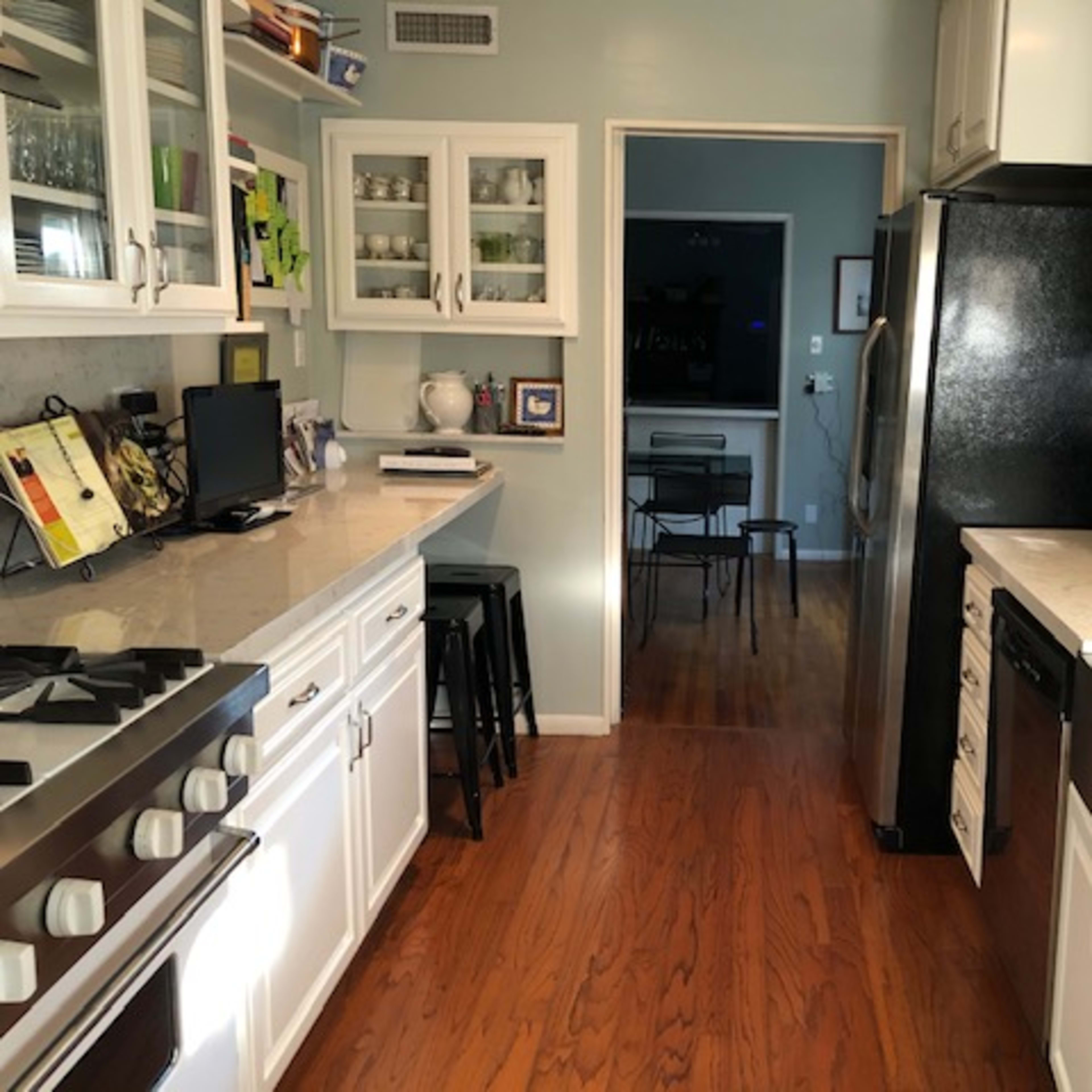 A bright kitchen features white cabinets, a black refrigerator, a stainless steel sink, and a dining area visible in the background.