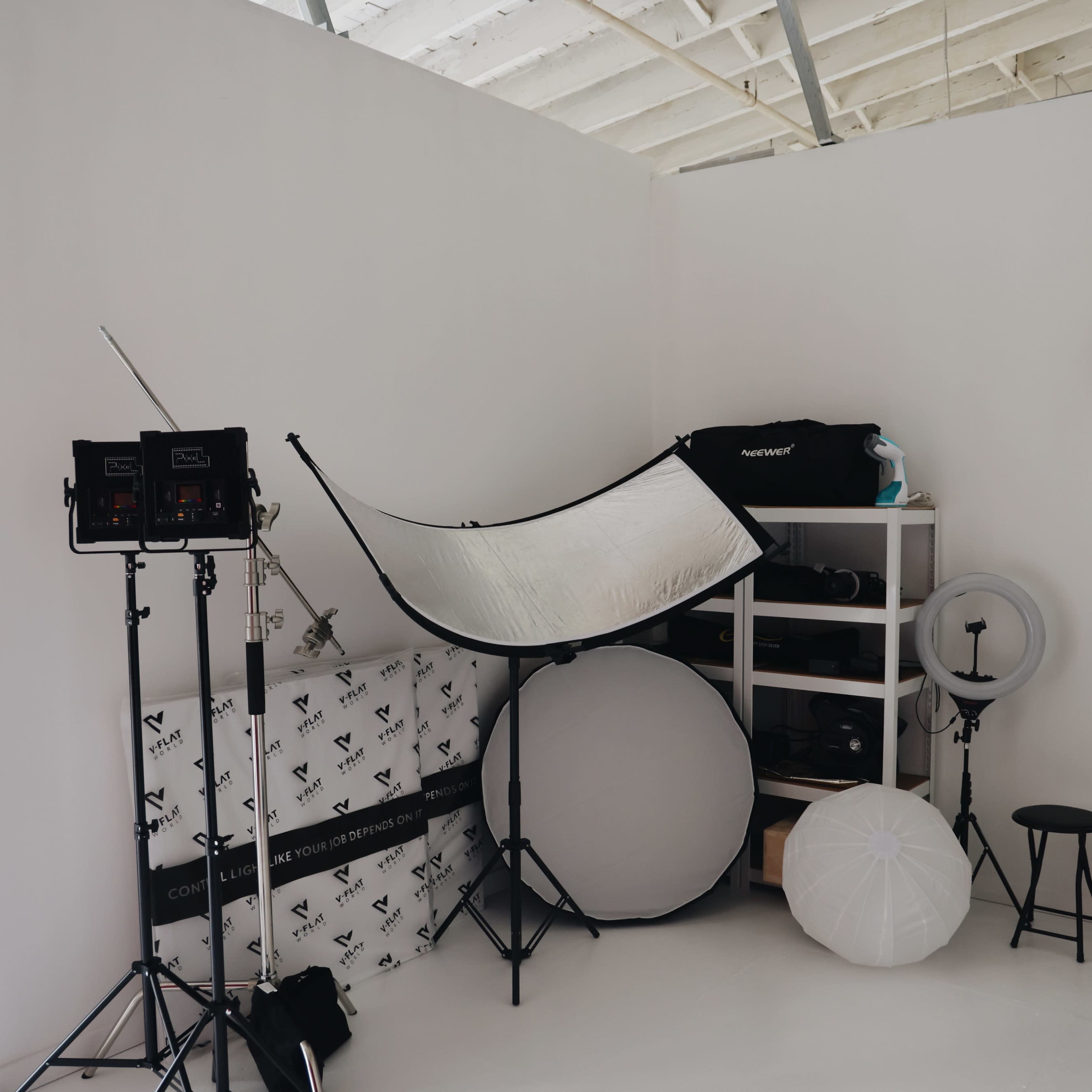 A photography studio corner with lighting equipment, reflectors, and a shelving unit filled with camera gear.