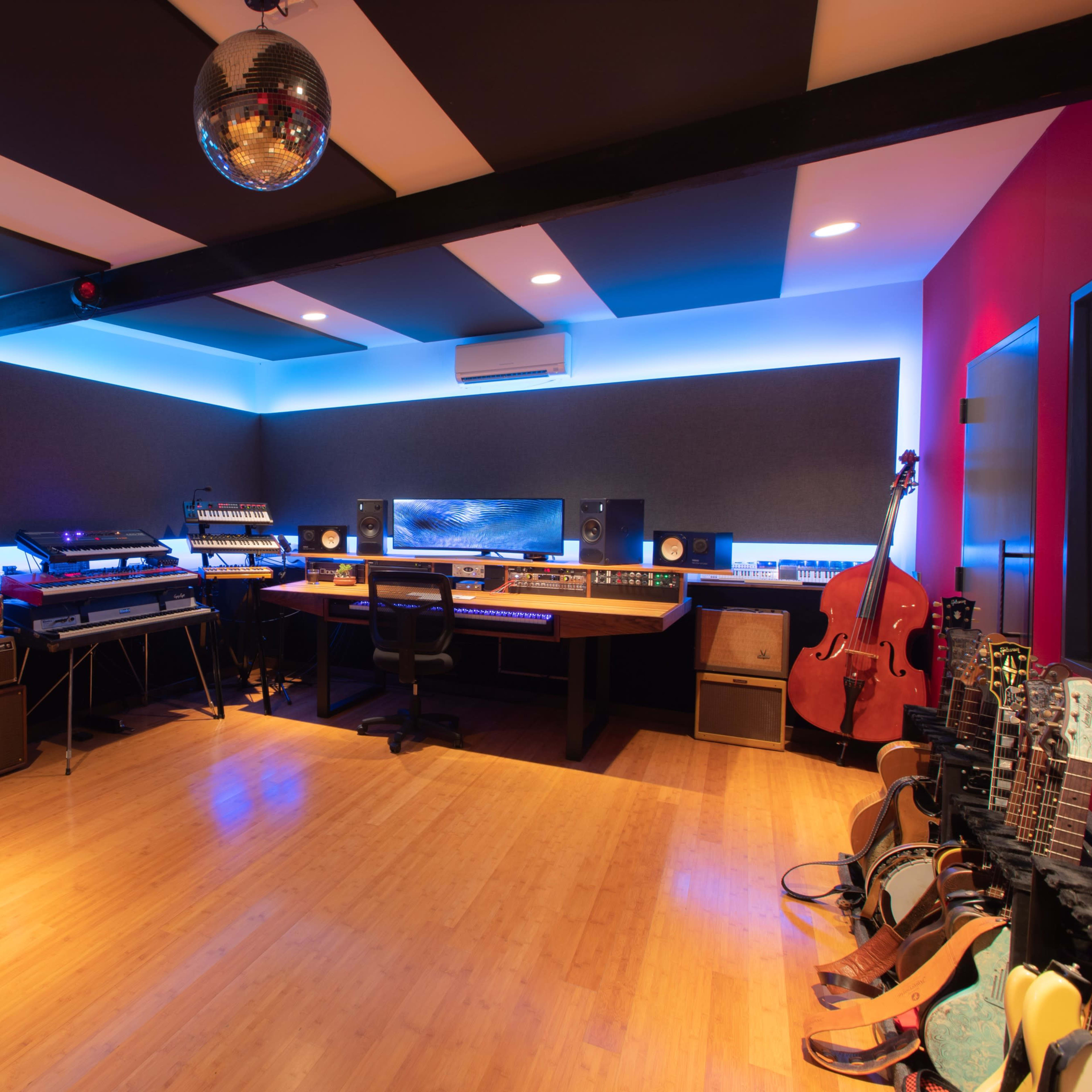 A modern music studio featuring various electronic instruments, acoustic panels, a central mixing desk, and ambient lighting.