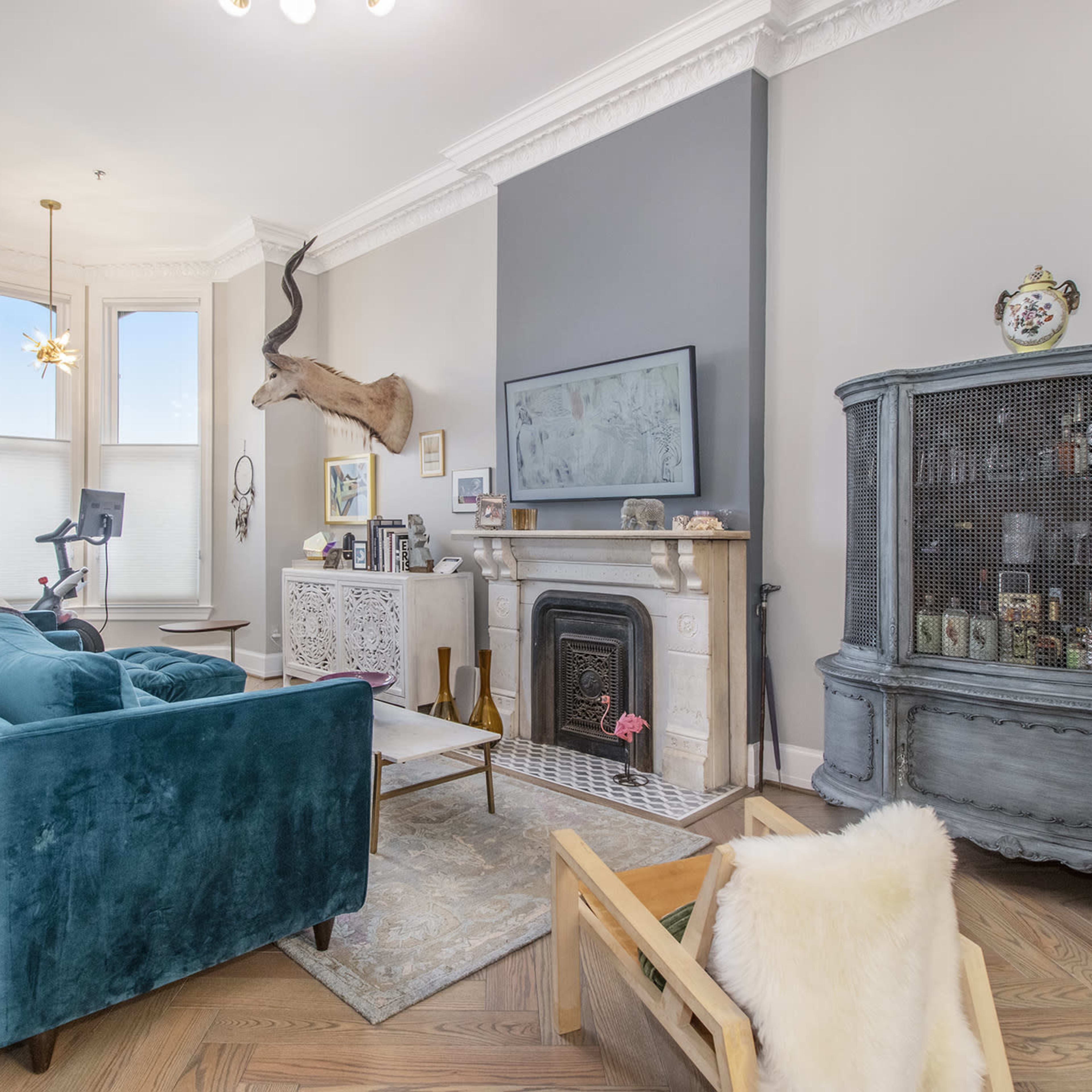 The living room features a teal sofa, a mounted deer head on the wall, a vintage cabinet, and a fireplace surrounded by decorative items.