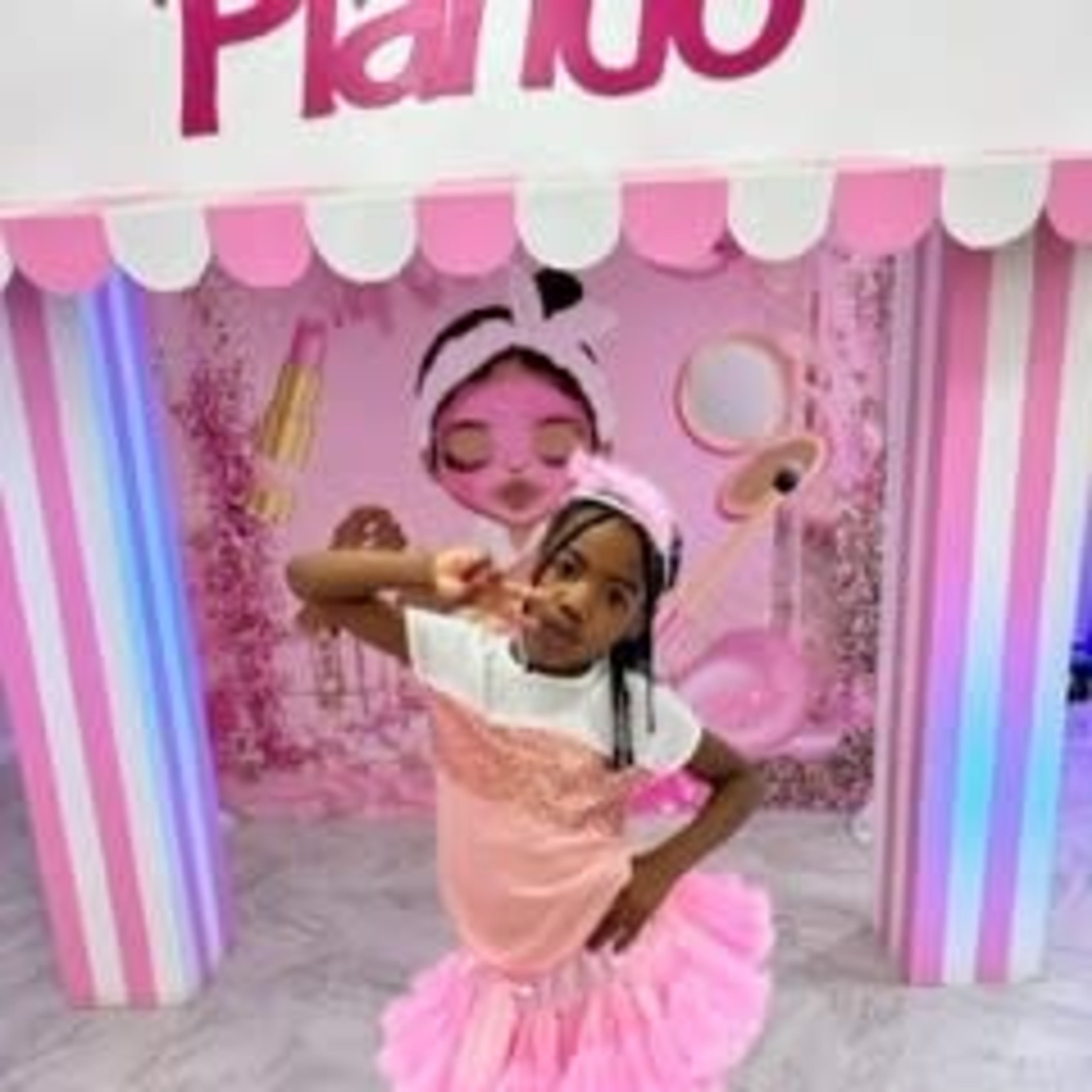 A child poses playfully in front of a colorful, pink-themed backdrop featuring makeup elements.