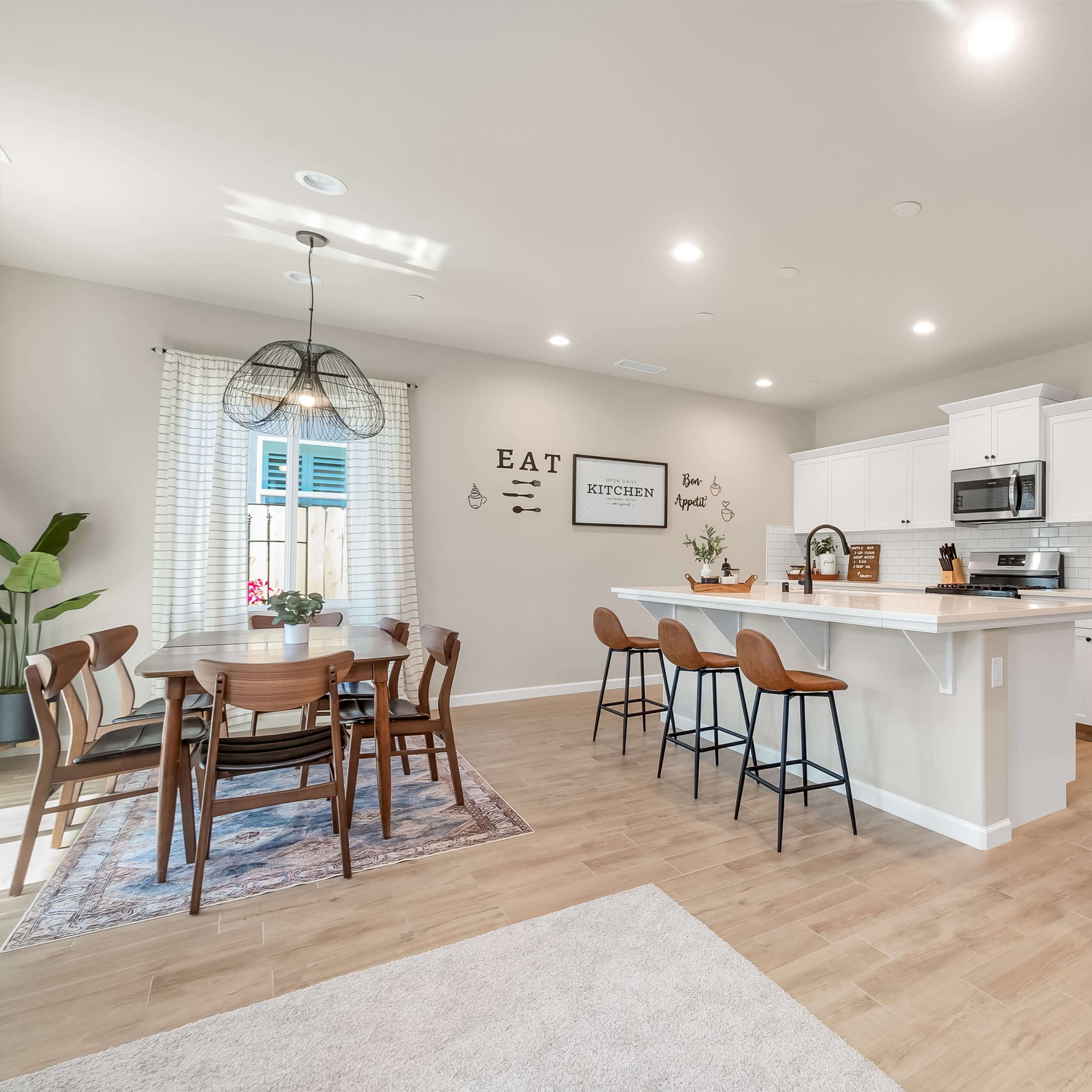 A modern kitchen and dining area features a wooden table, bar seating, stainless steel appliances, and light-colored cabinetry.