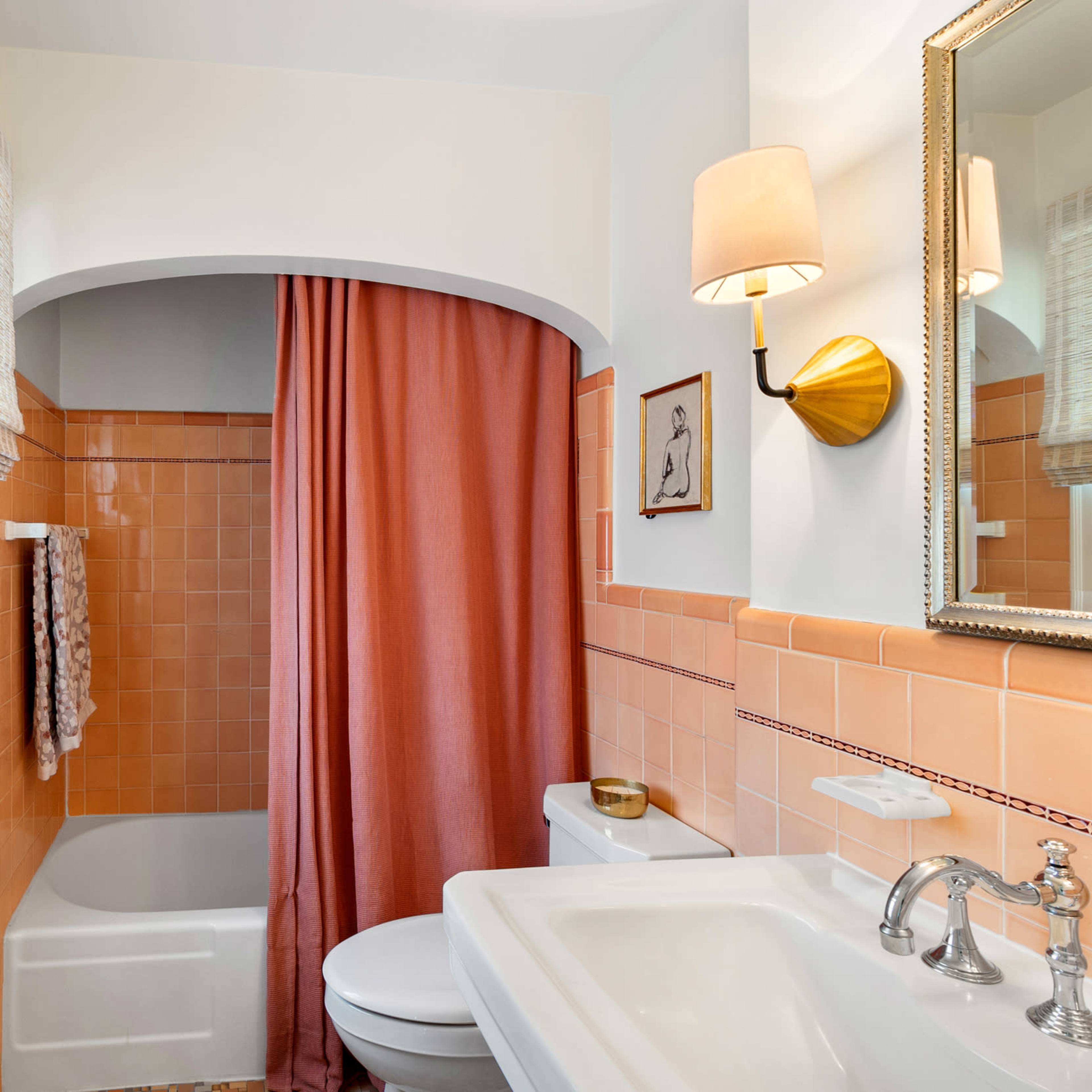 The bathroom features a tub with a pink curtain, tiled walls, a sink, and a gold wall sconce.