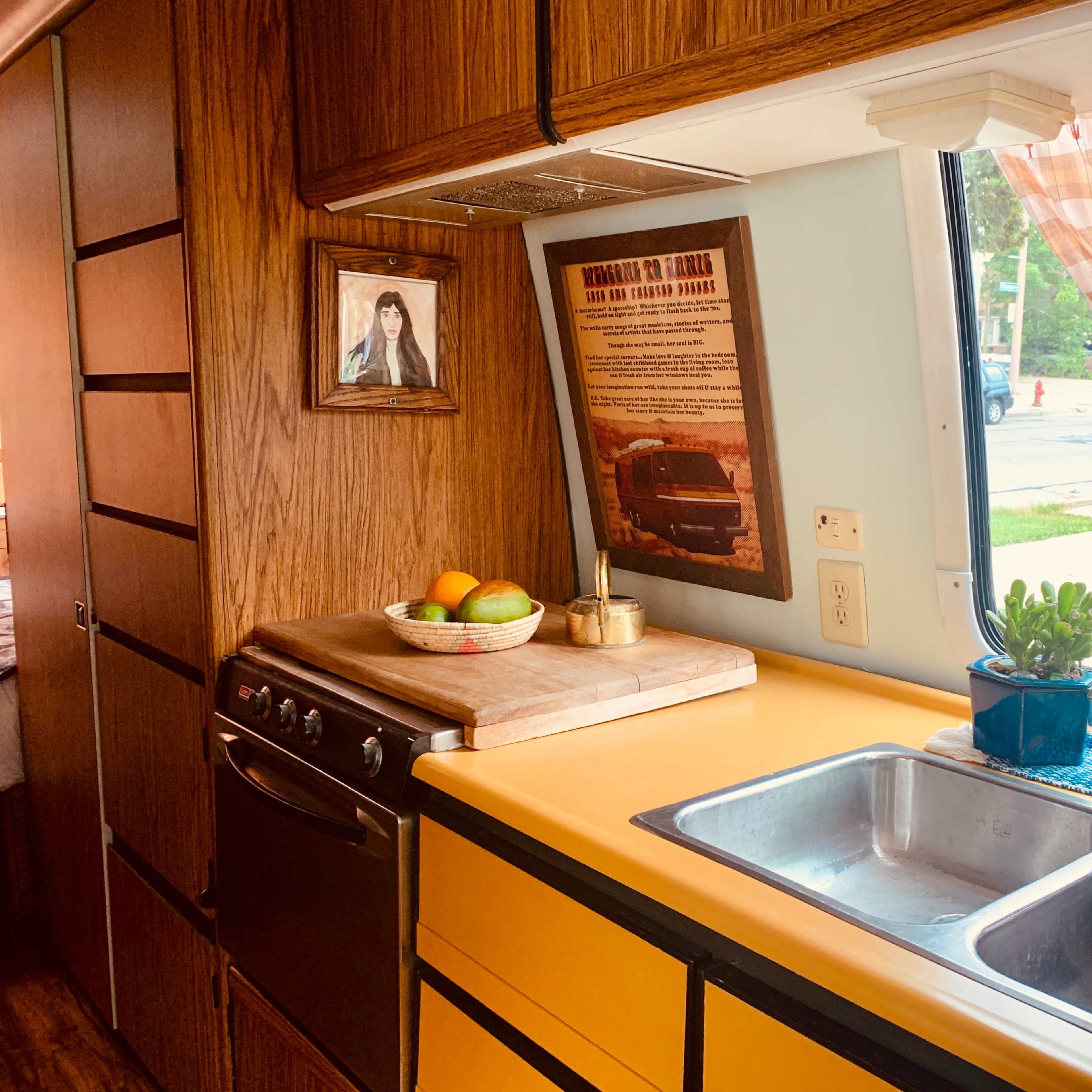 A kitchen interior with wooden cabinets, a yellow countertop, a double sink, and a framed picture on the wall.