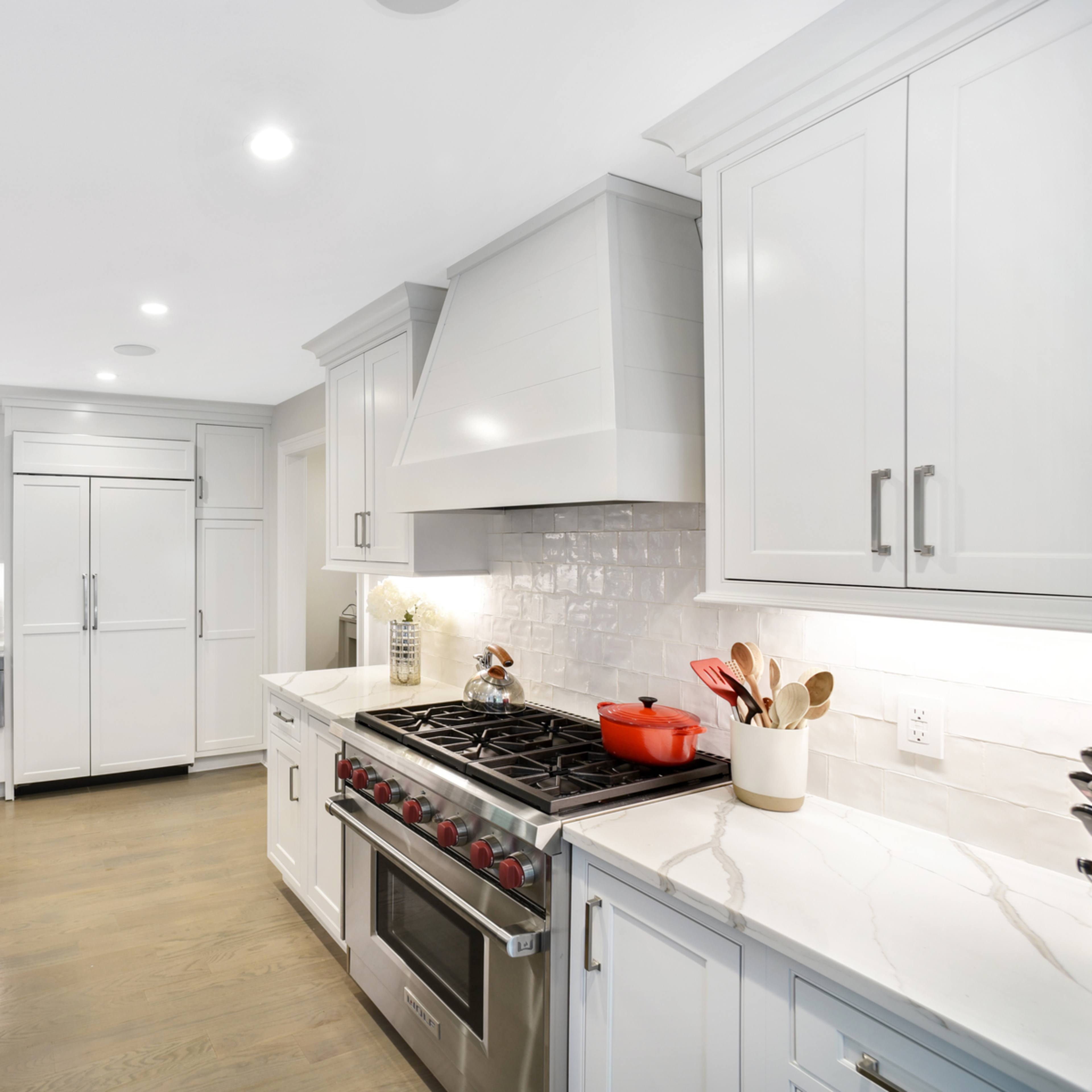 The kitchen features white cabinetry, a large central island with a sink, stainless steel appliances, and a gas range.