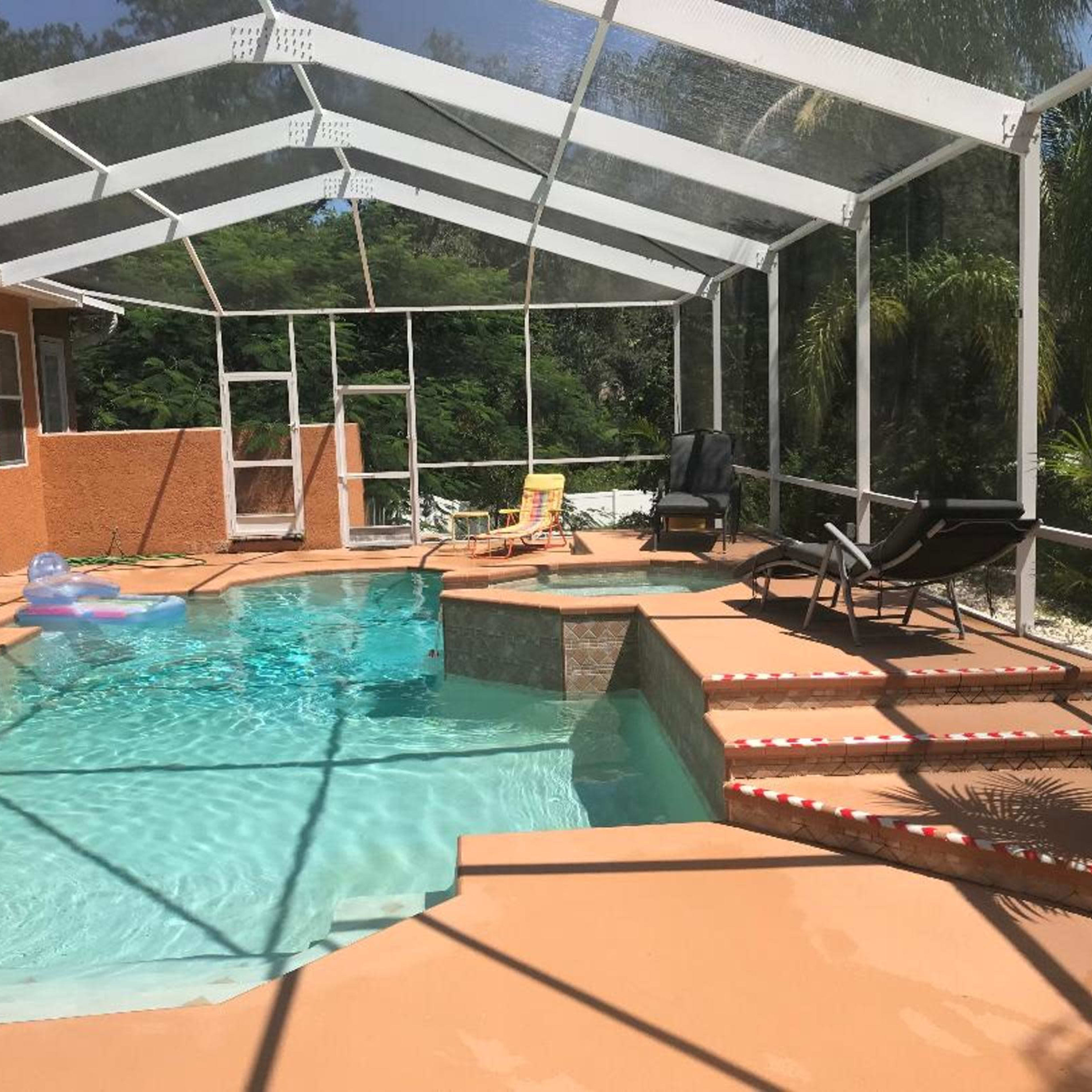 A screened-in pool area with a blue swimming pool, chaise lounges, and surrounding greenery.