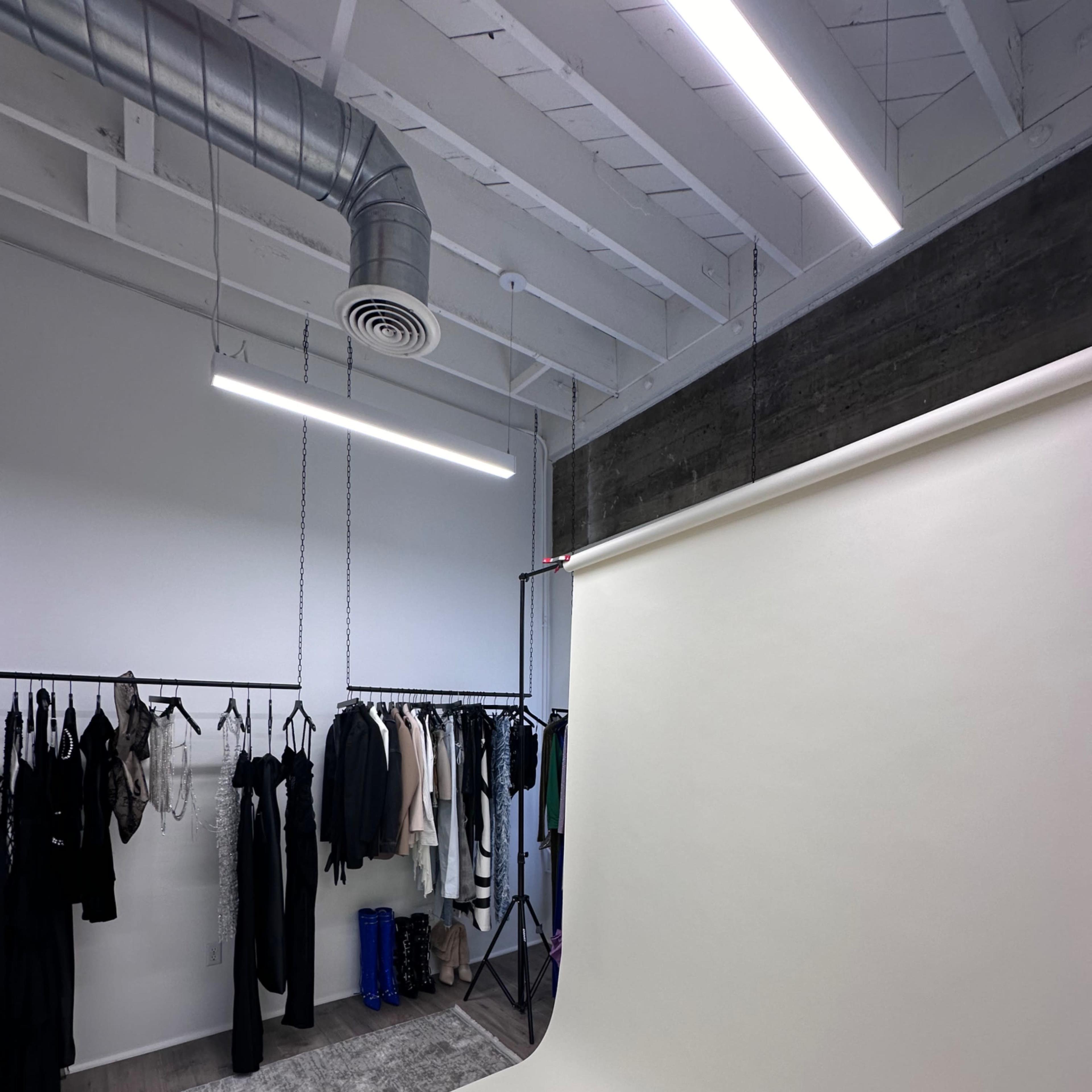 A photography studio with a seamless backdrop, hanging clothing on racks, and overhead lighting.
