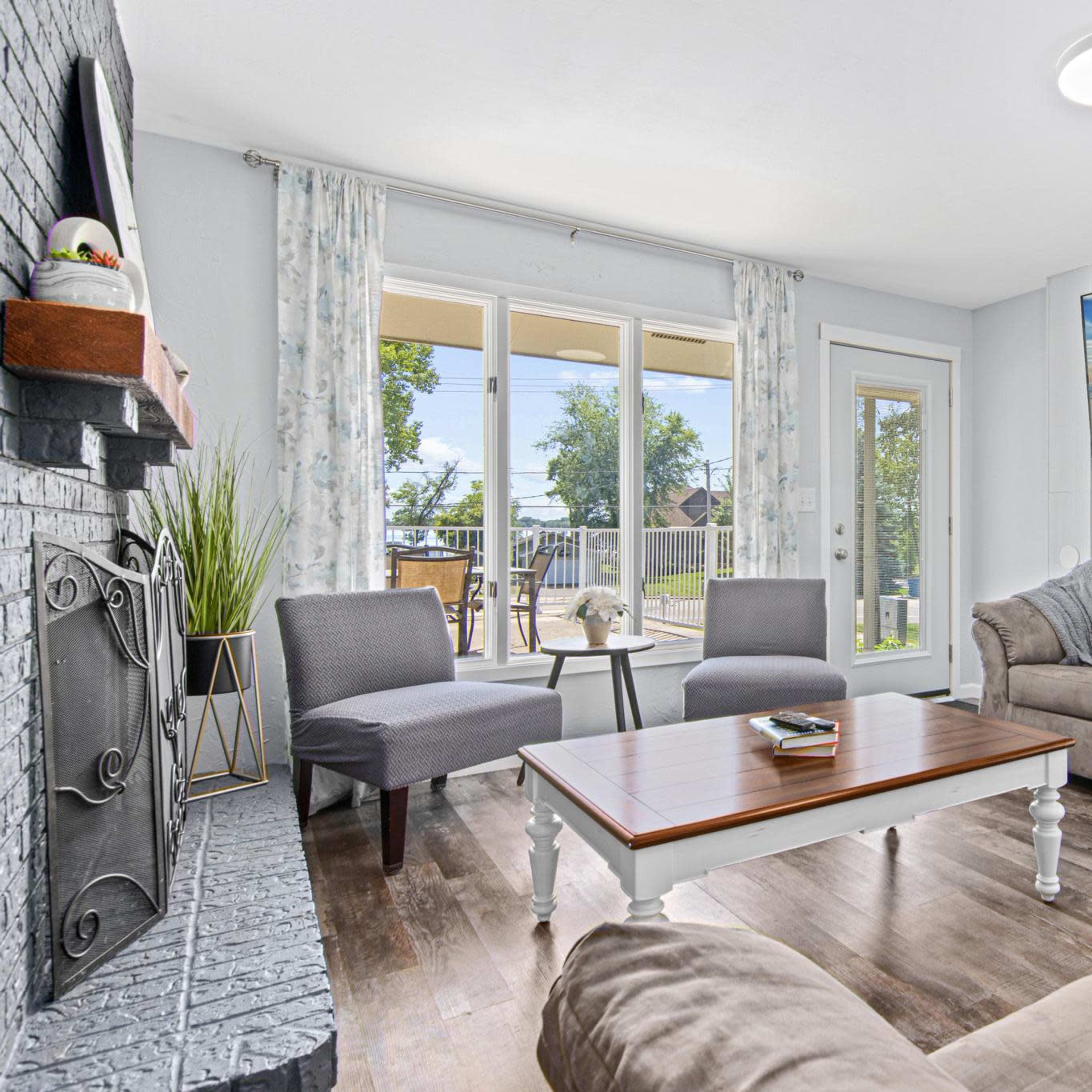 A cozy living room features a large sectional sofa, two armchairs, a wooden coffee table, and a mounted television, with large windows letting in natural light.