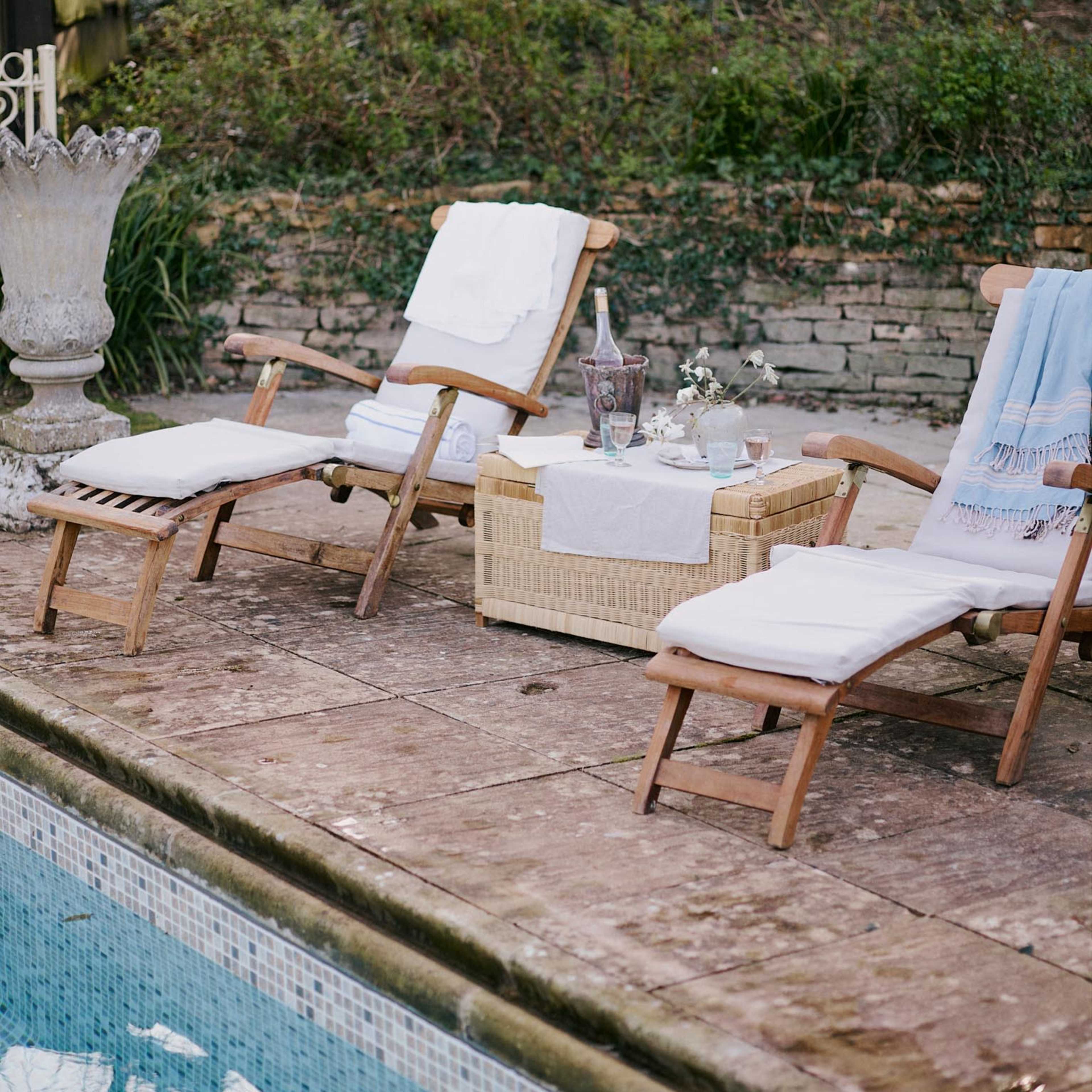 Lounge chairs are positioned beside a swimming pool, with a wicker table displaying drinks and a floral arrangement.