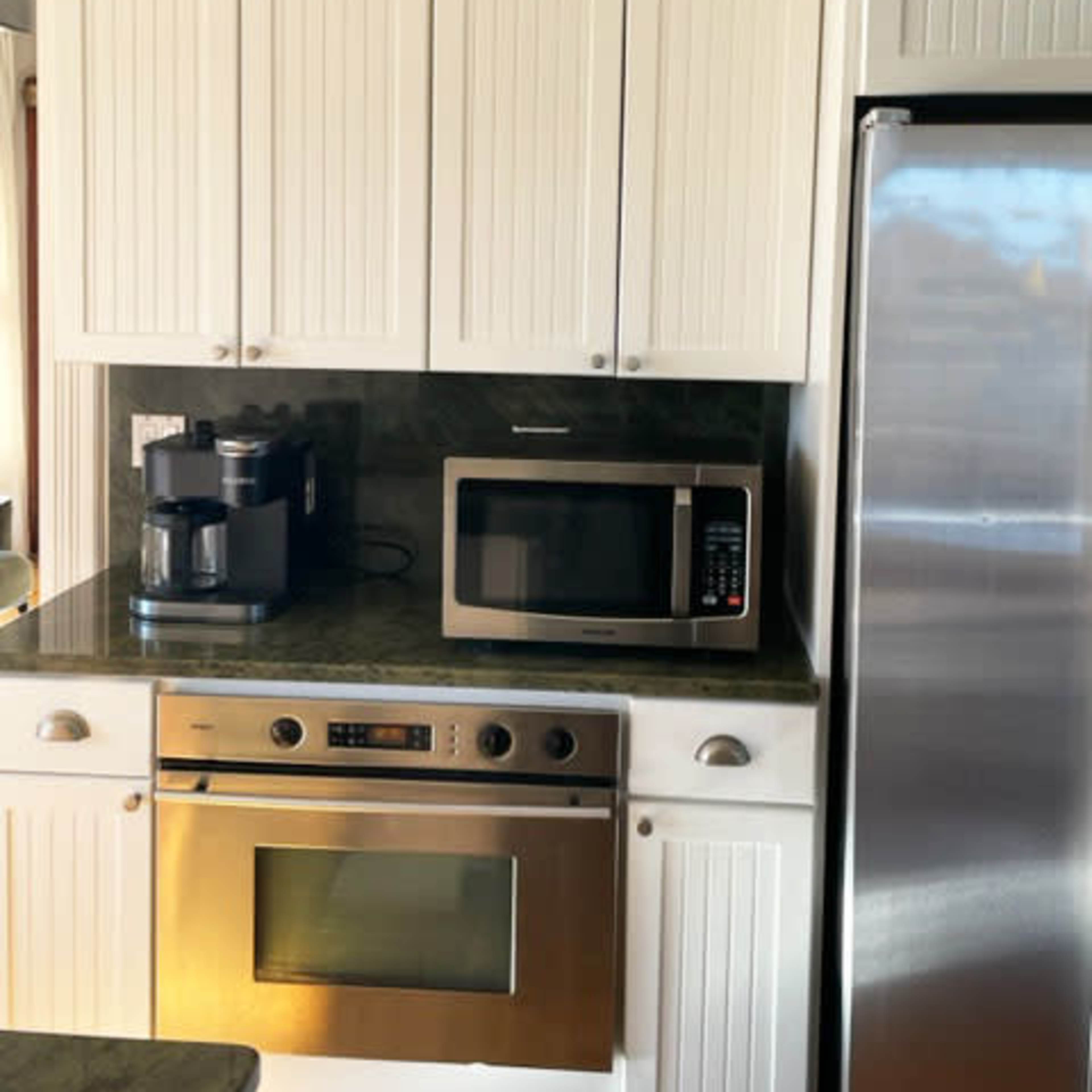 A kitchen area featuring white cabinets, a microwave, an oven, and a stainless steel refrigerator.