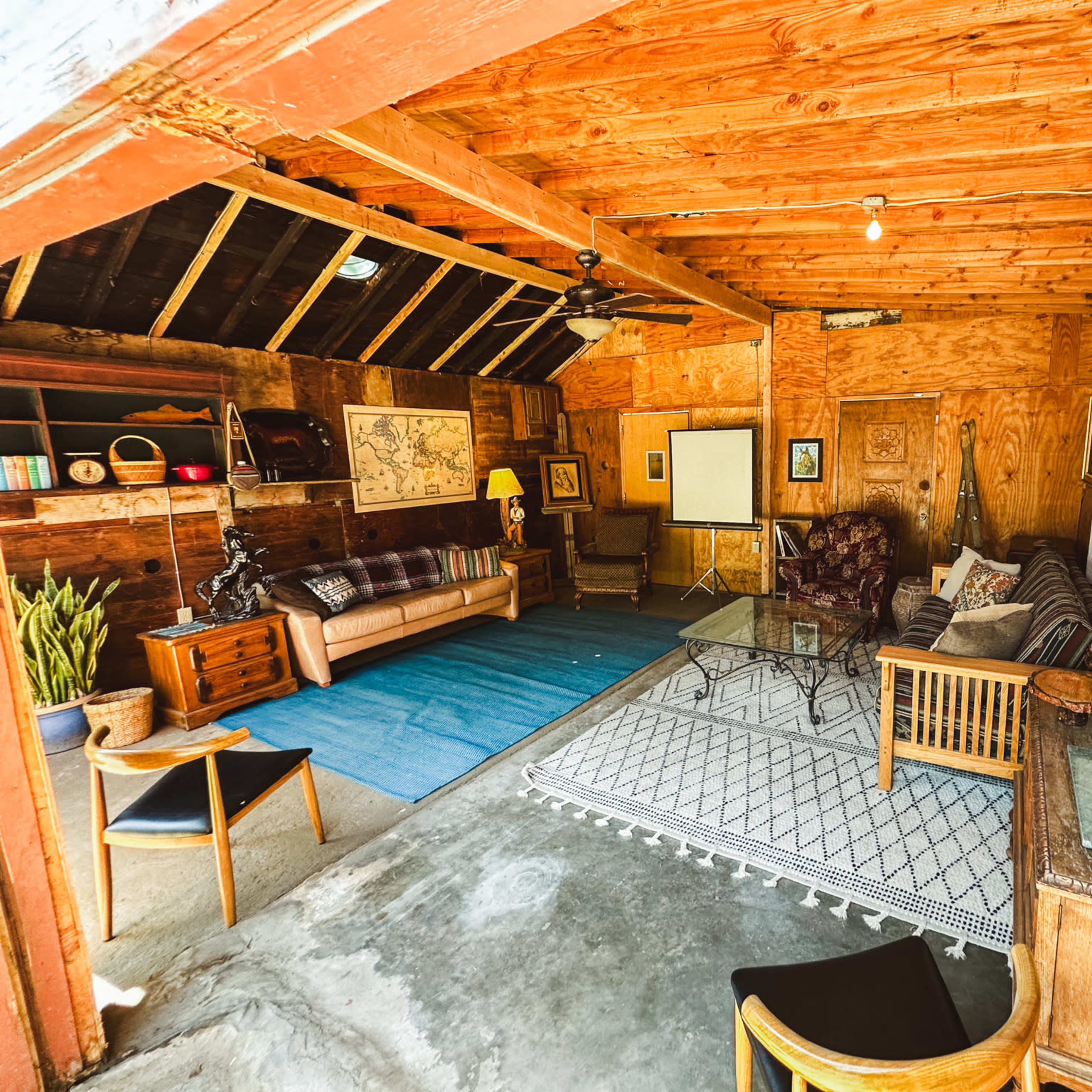 A rustic interior of a living space with wooden beams, a mix of furniture, and decorative items, including a large map and plants.