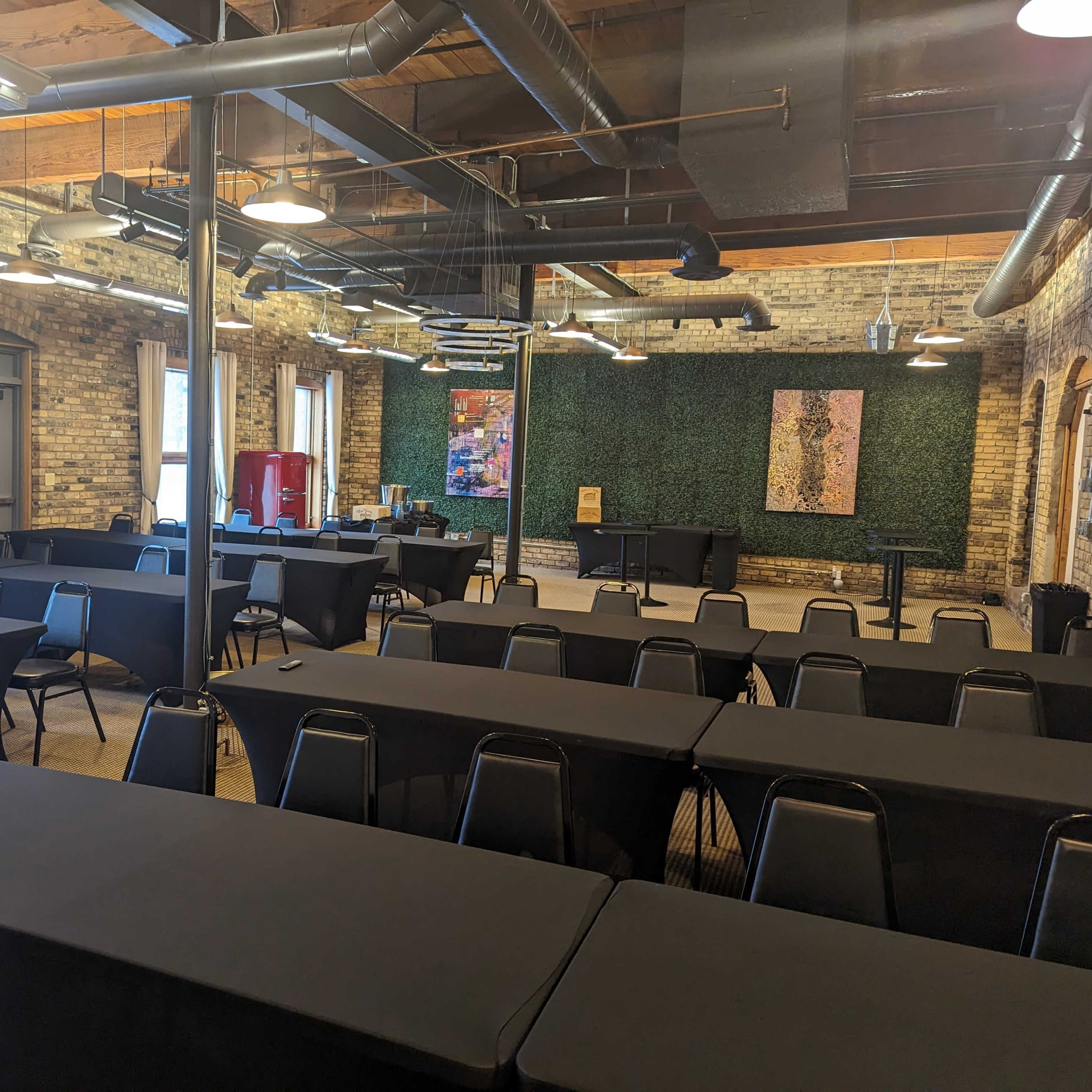 A large meeting room with several rows of tables covered in black tablecloths and a green wall featuring artwork in the background.