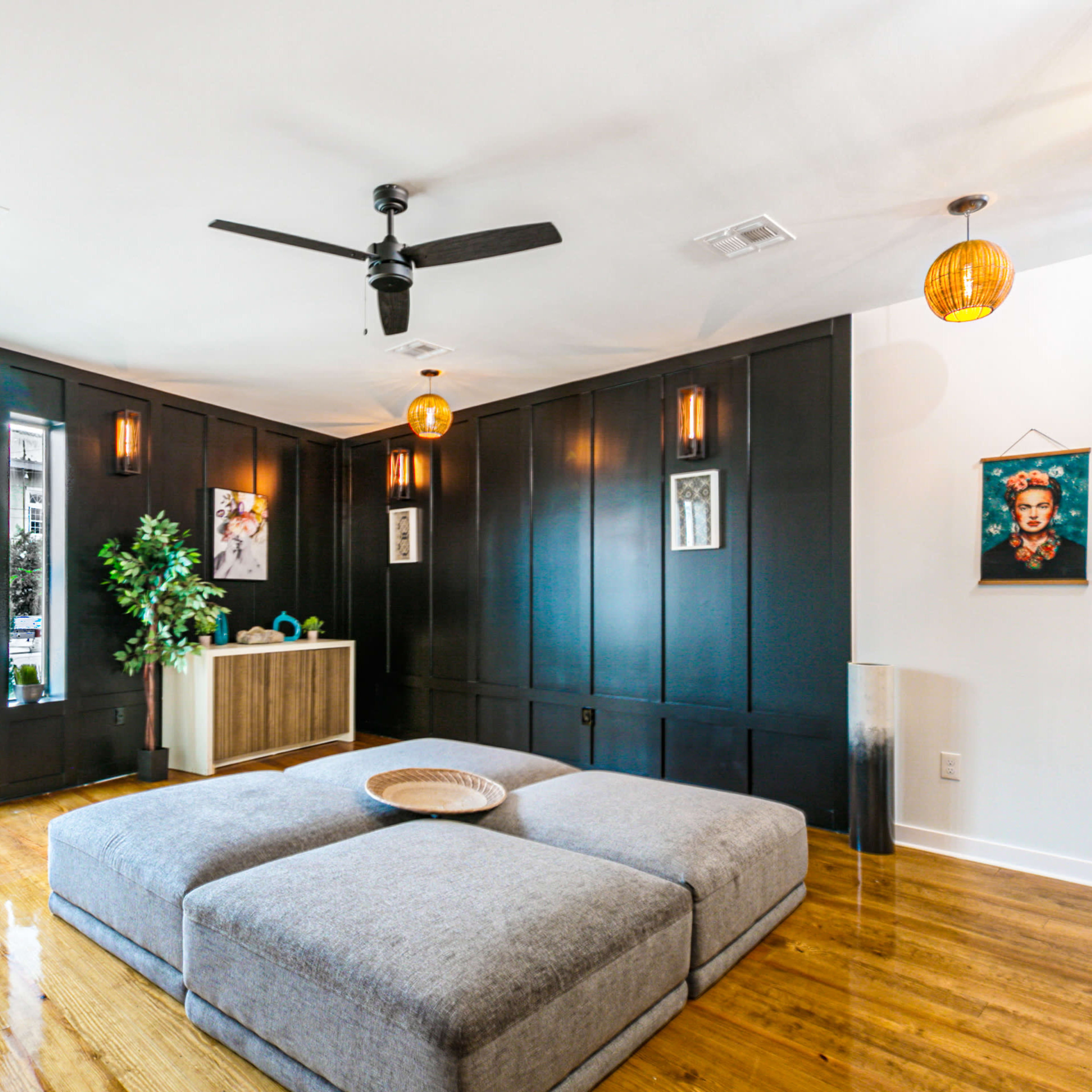 The living room features a large gray sectional ottoman, dark paneled walls, and decorative pendant lights.