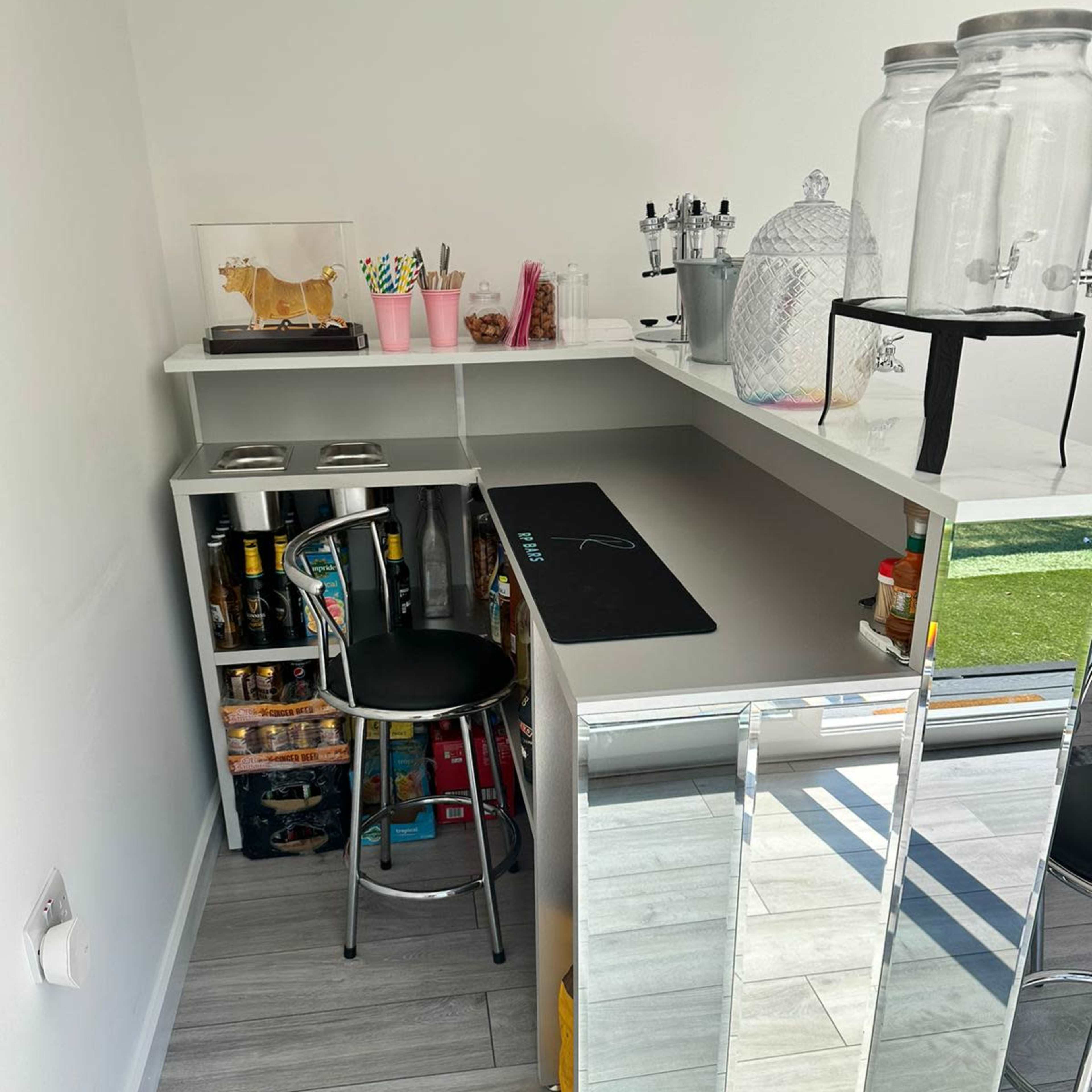 A small, modern bar area with a sleek countertop, black stool, and organized shelves filled with snacks and beverages.