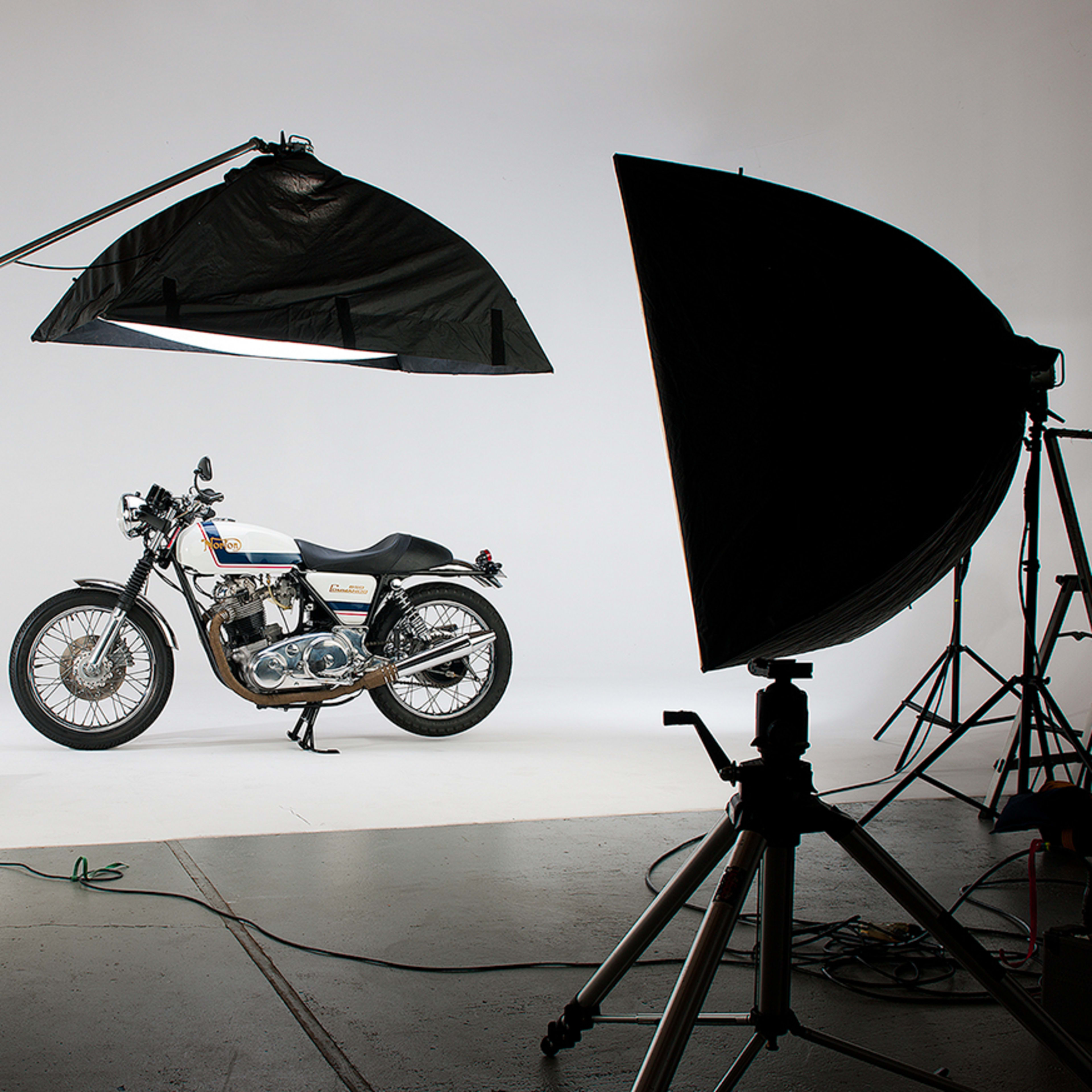 A motorcycle is positioned on a white backdrop, flanked by large light modifiers and photography equipment.