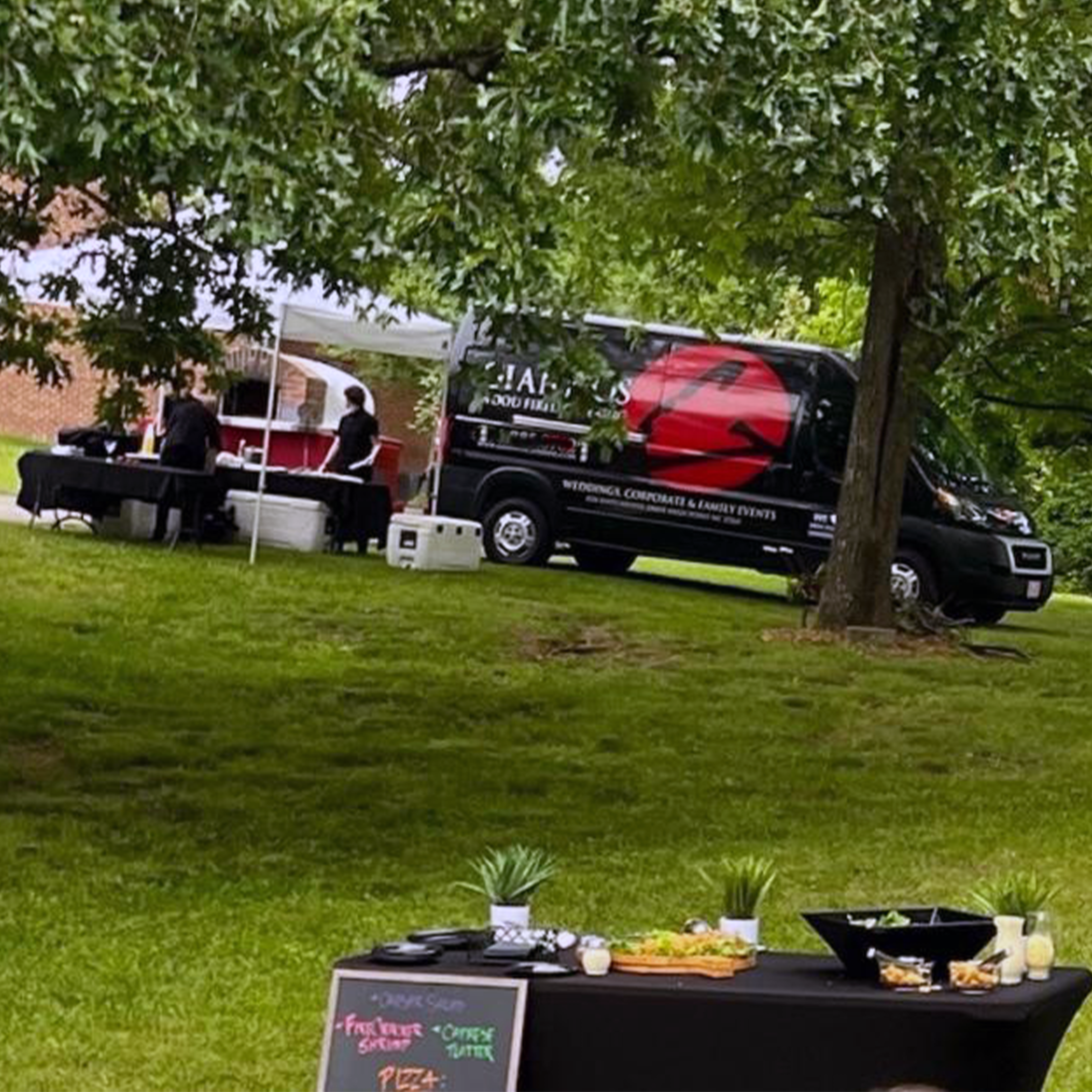 A food truck is parked next to a canopy with tables set up on a grassy lawn.