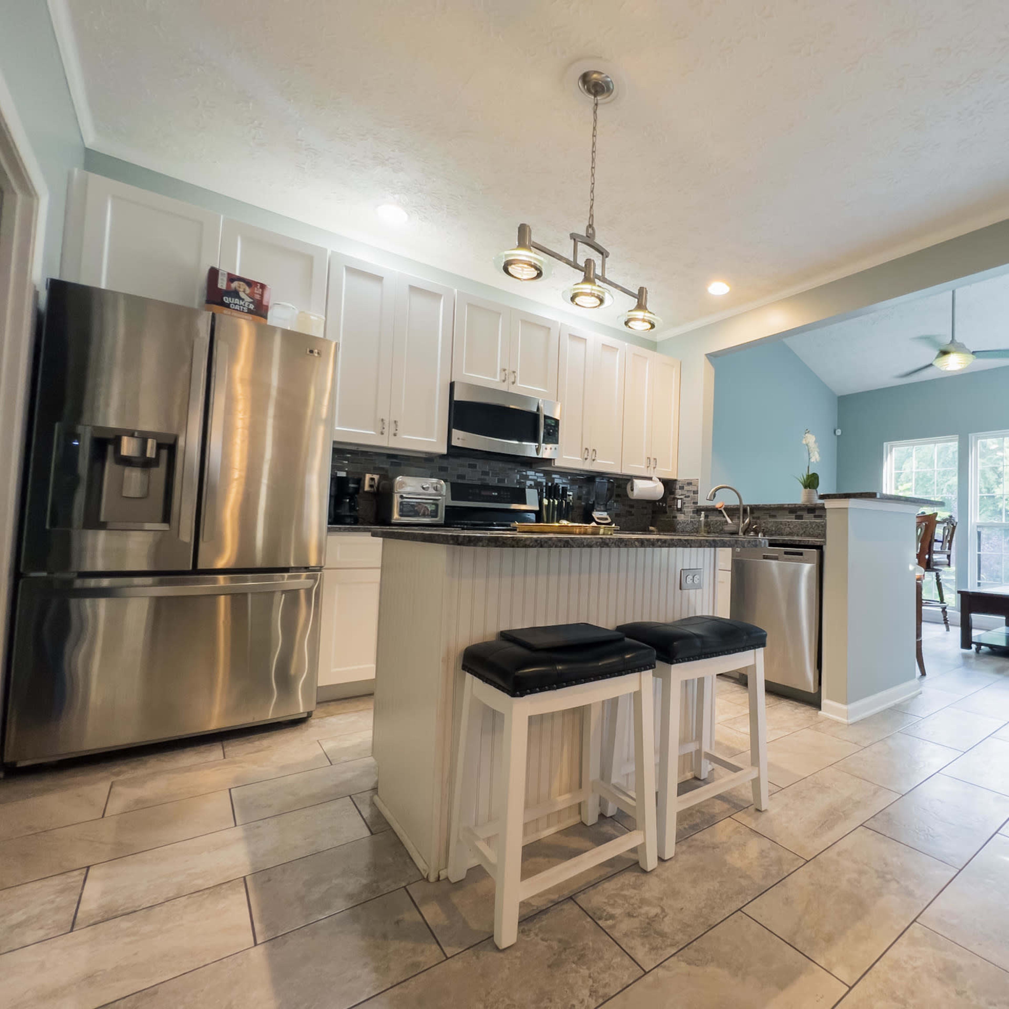 A modern kitchen with stainless steel appliances, a central island with seating, and an open living area featuring a couch and large windows.