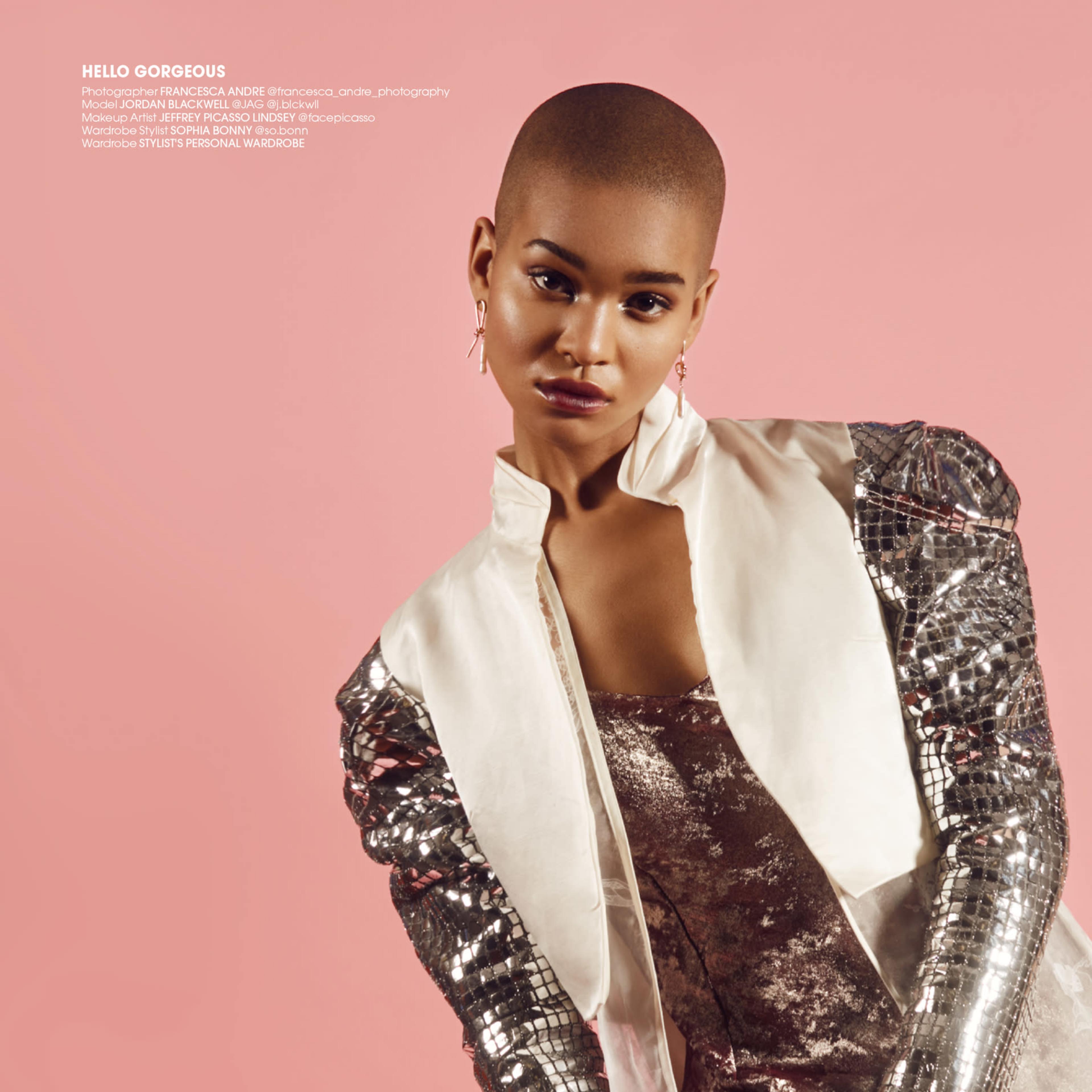 A model poses in a sparkling silver outfit against a pink background.