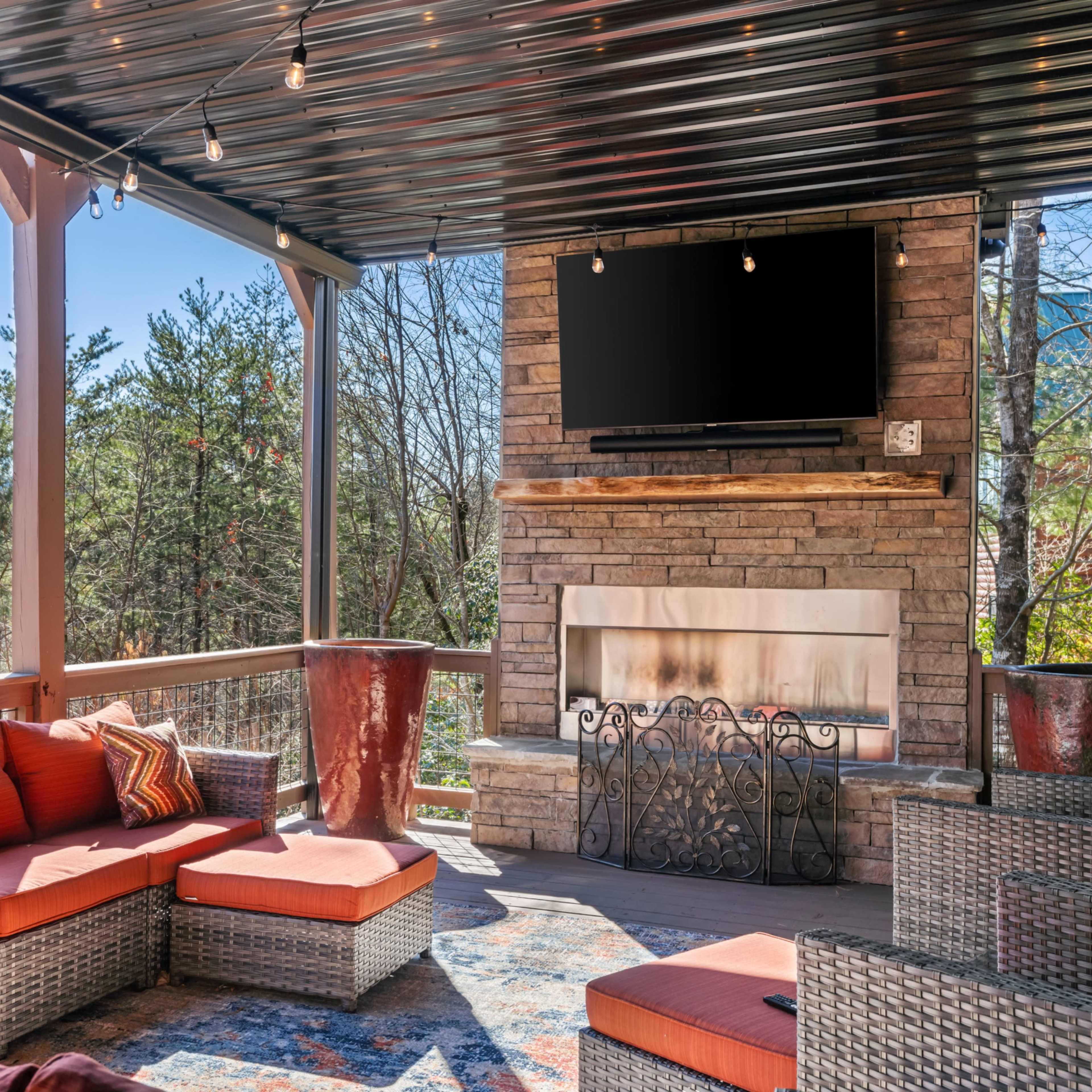 The outdoor living space features a sectional sofa, stone fireplace, and a mounted television under a covered patio.