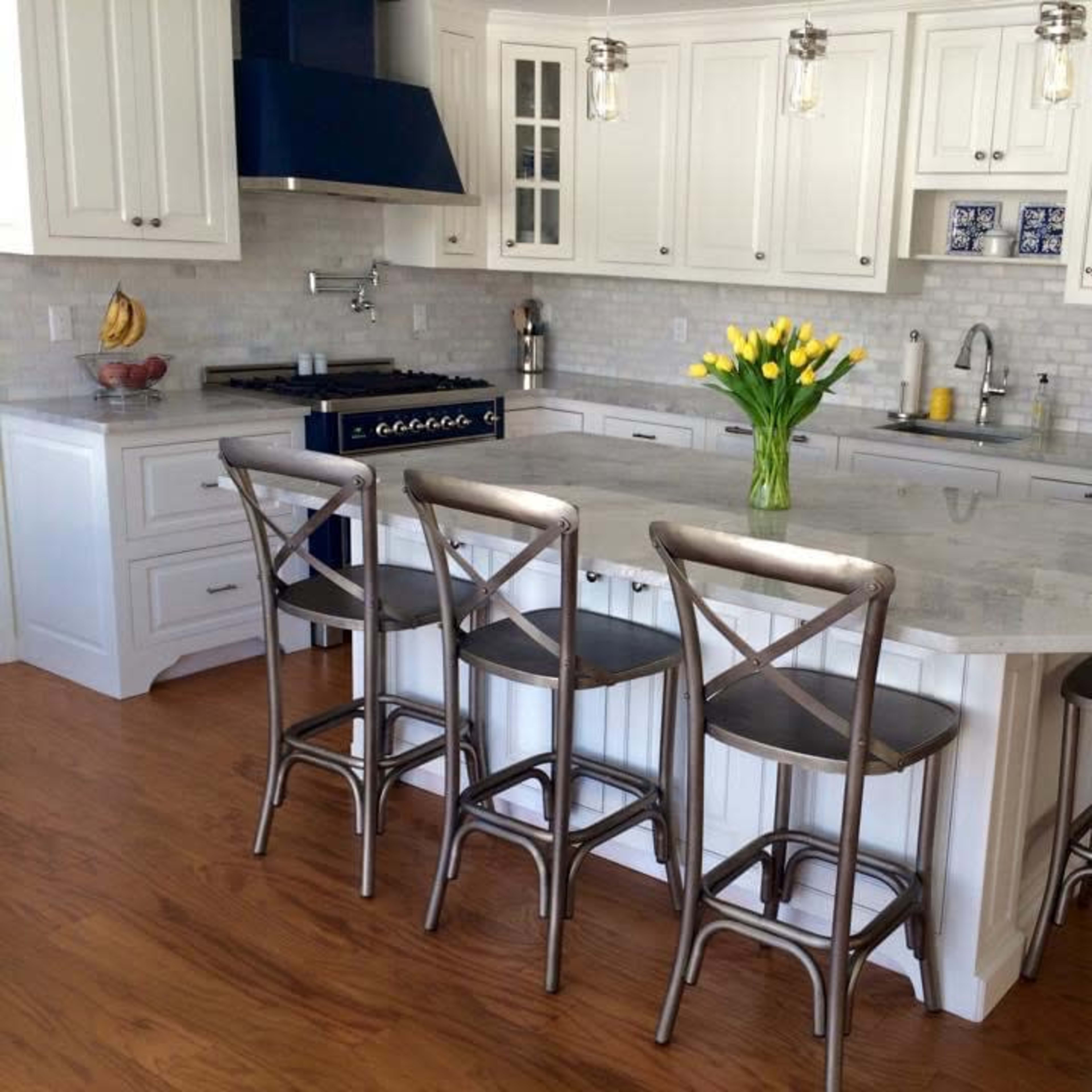 A modern kitchen features white cabinetry, a large marble island with seating, and a vase of yellow tulips at the center.