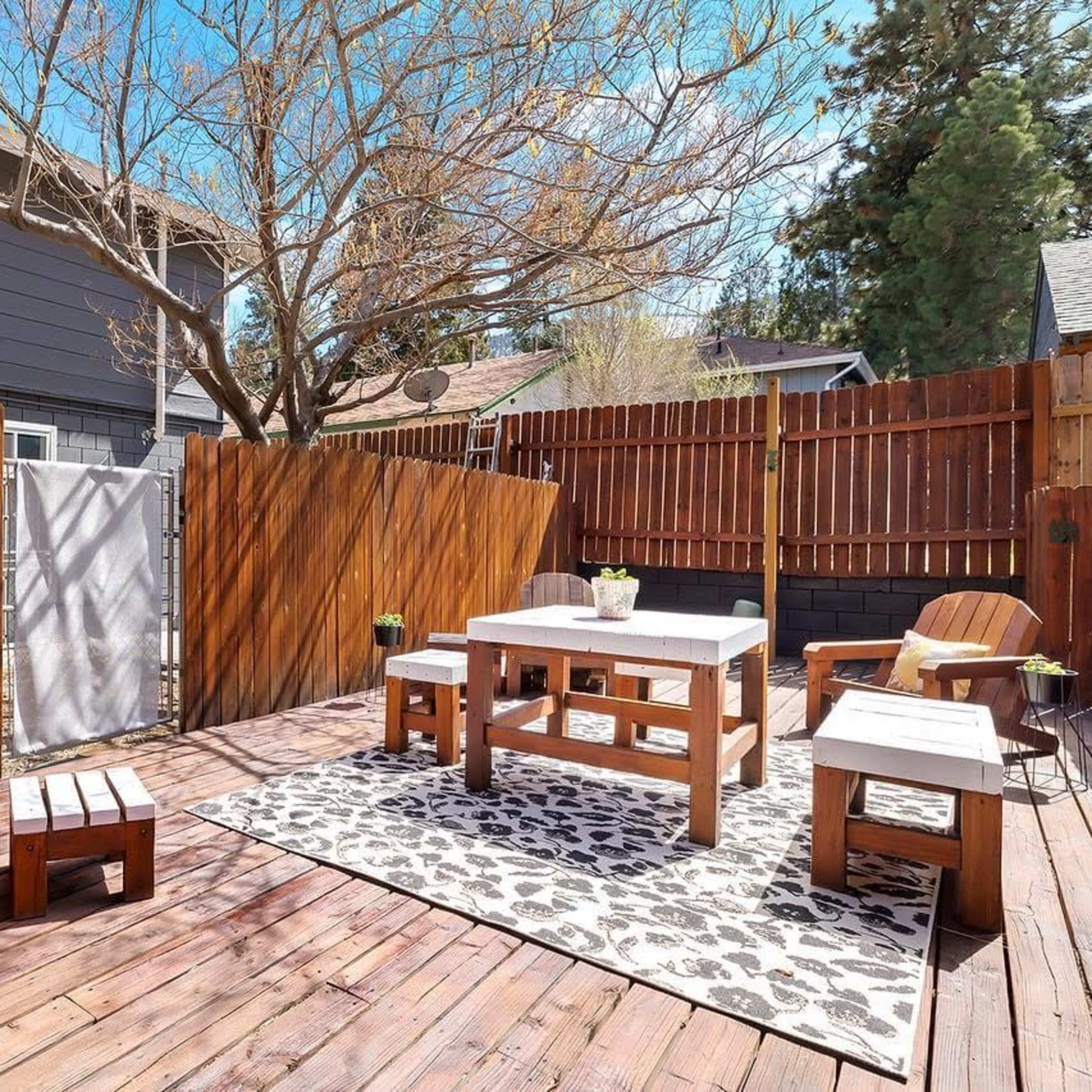 A wooden deck area with several seating arrangements, including chairs and tables, surrounded by wooden fencing and a bare tree.