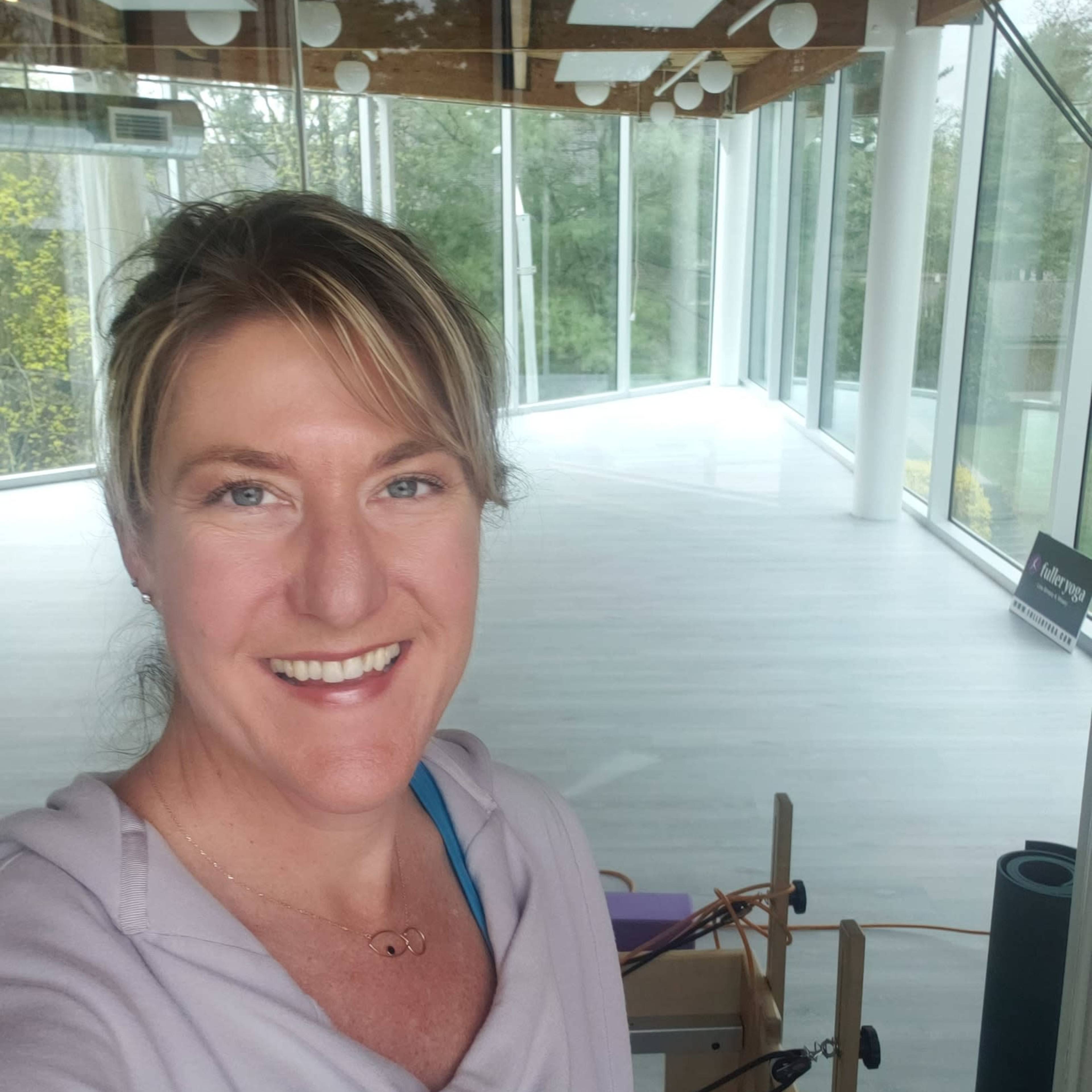 A woman smiles in a bright, modern studio with large windows and minimalistic decor.