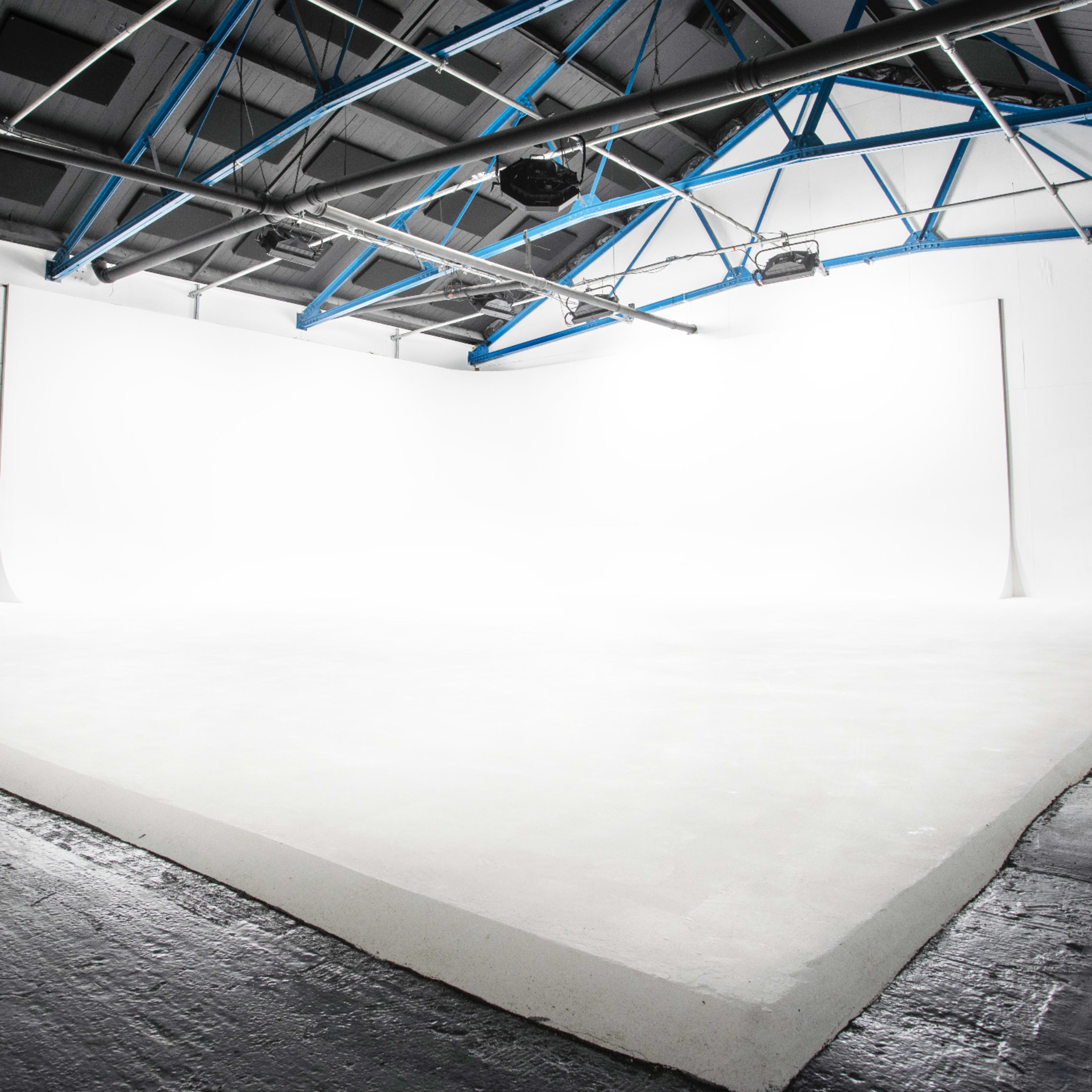 A spacious, well-lit studio with white walls and a sloped white floor.