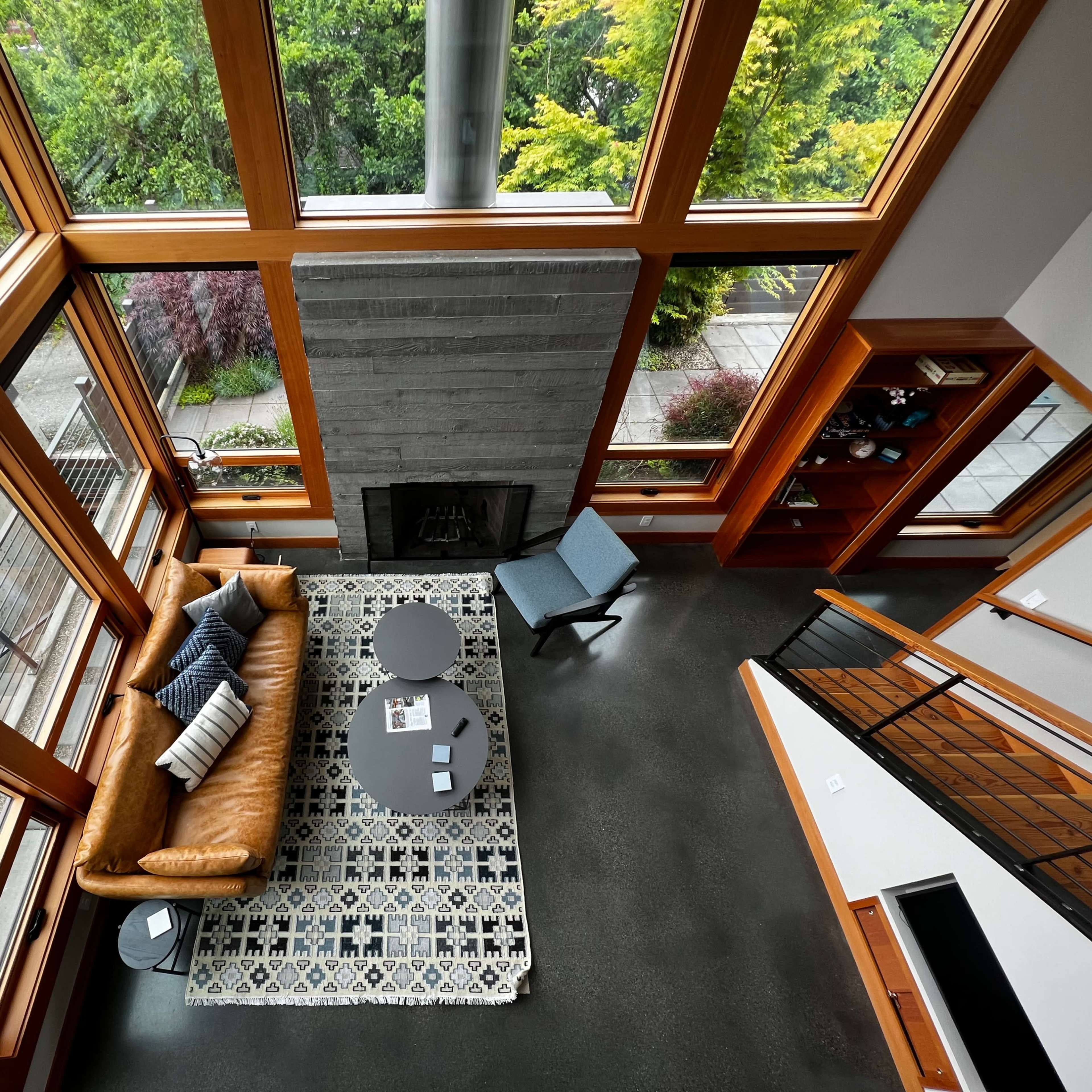 An open living space with large windows, a leather sofa, a patterned rug, and a modern fireplace, allowing natural light to fill the room.