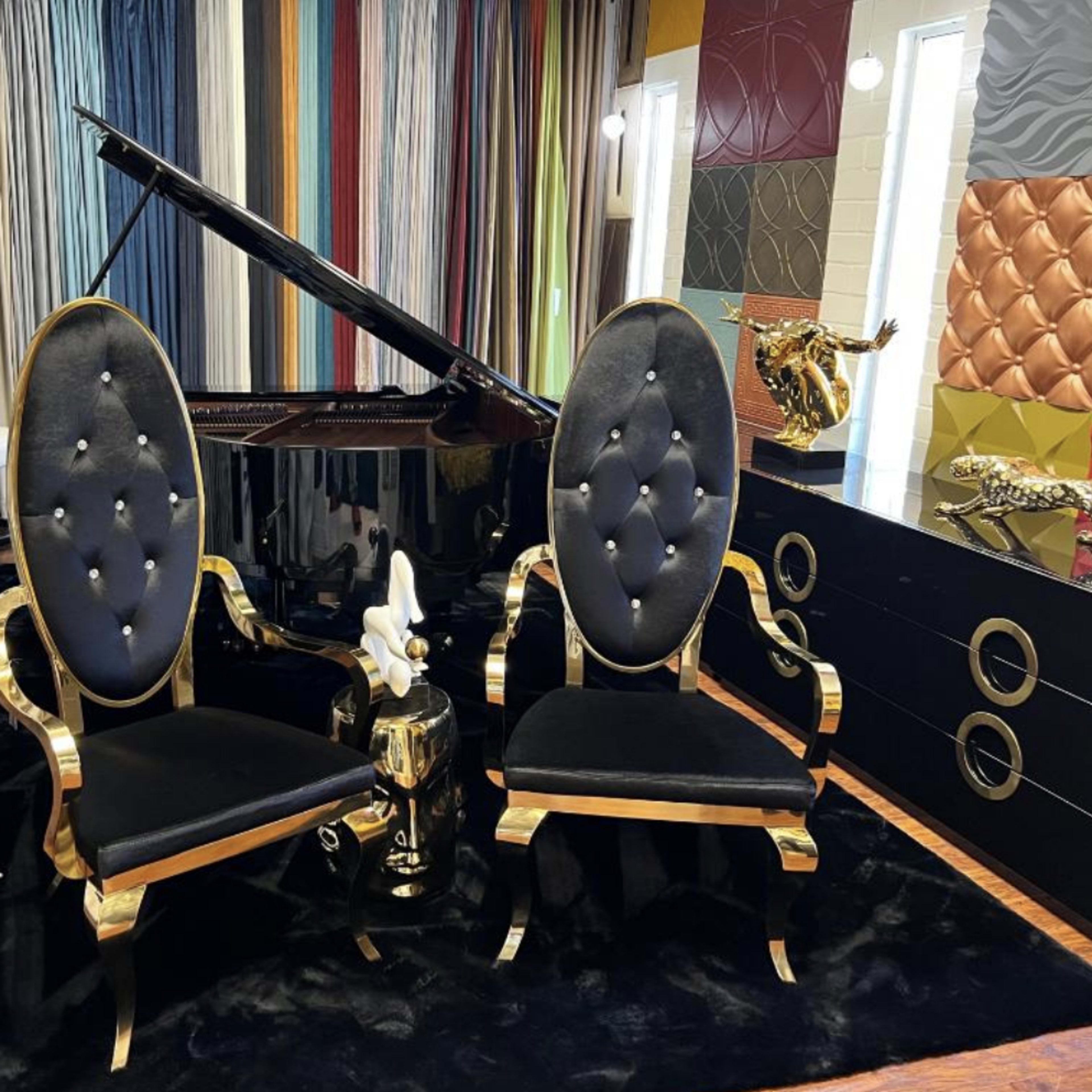 Two ornate black and gold chairs are positioned in front of a grand piano, accompanied by a decorative sculpture and a colorful wall display.