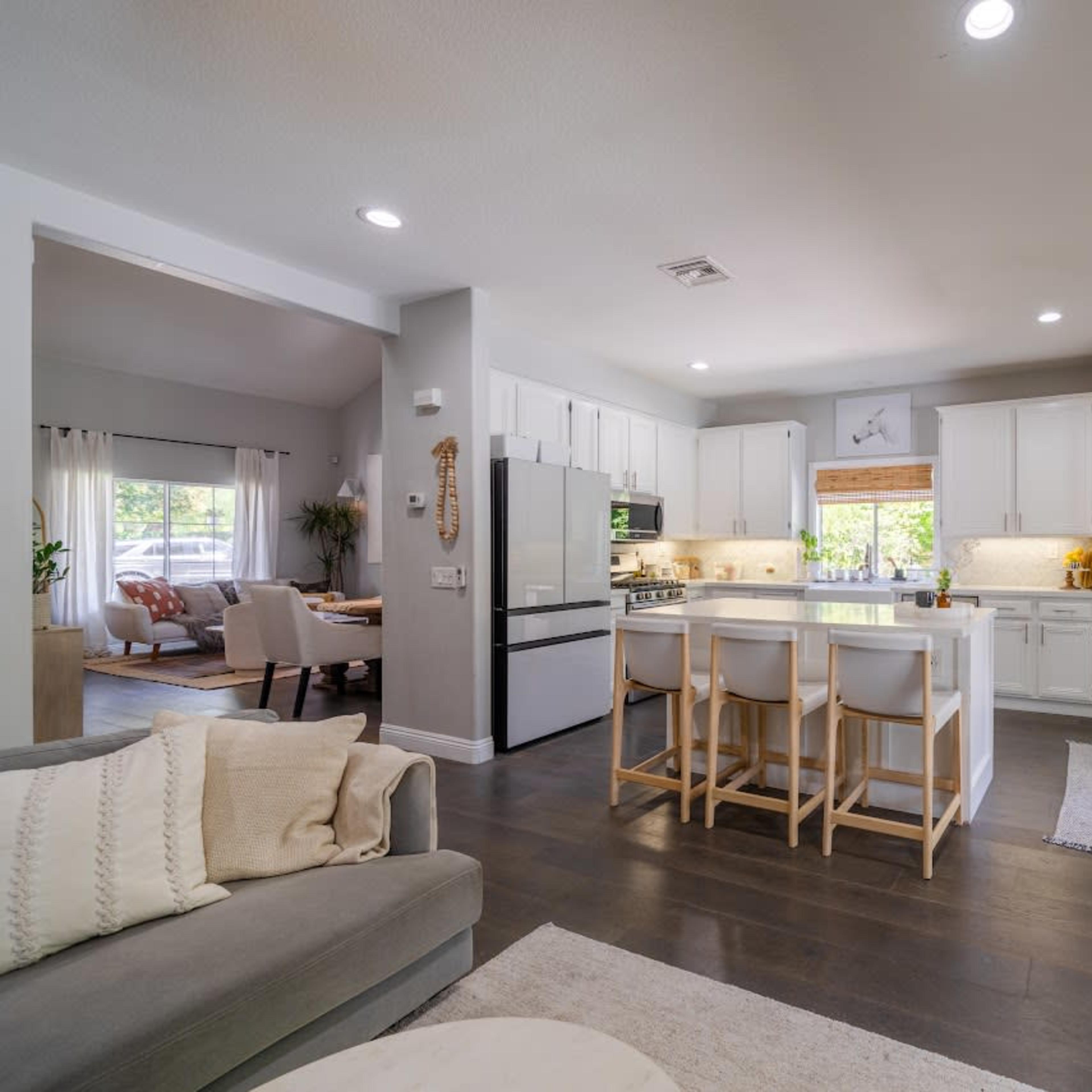 A modern kitchen with white cabinetry, an island with bar stools, and an open layout connecting to a living area with a seating arrangement.