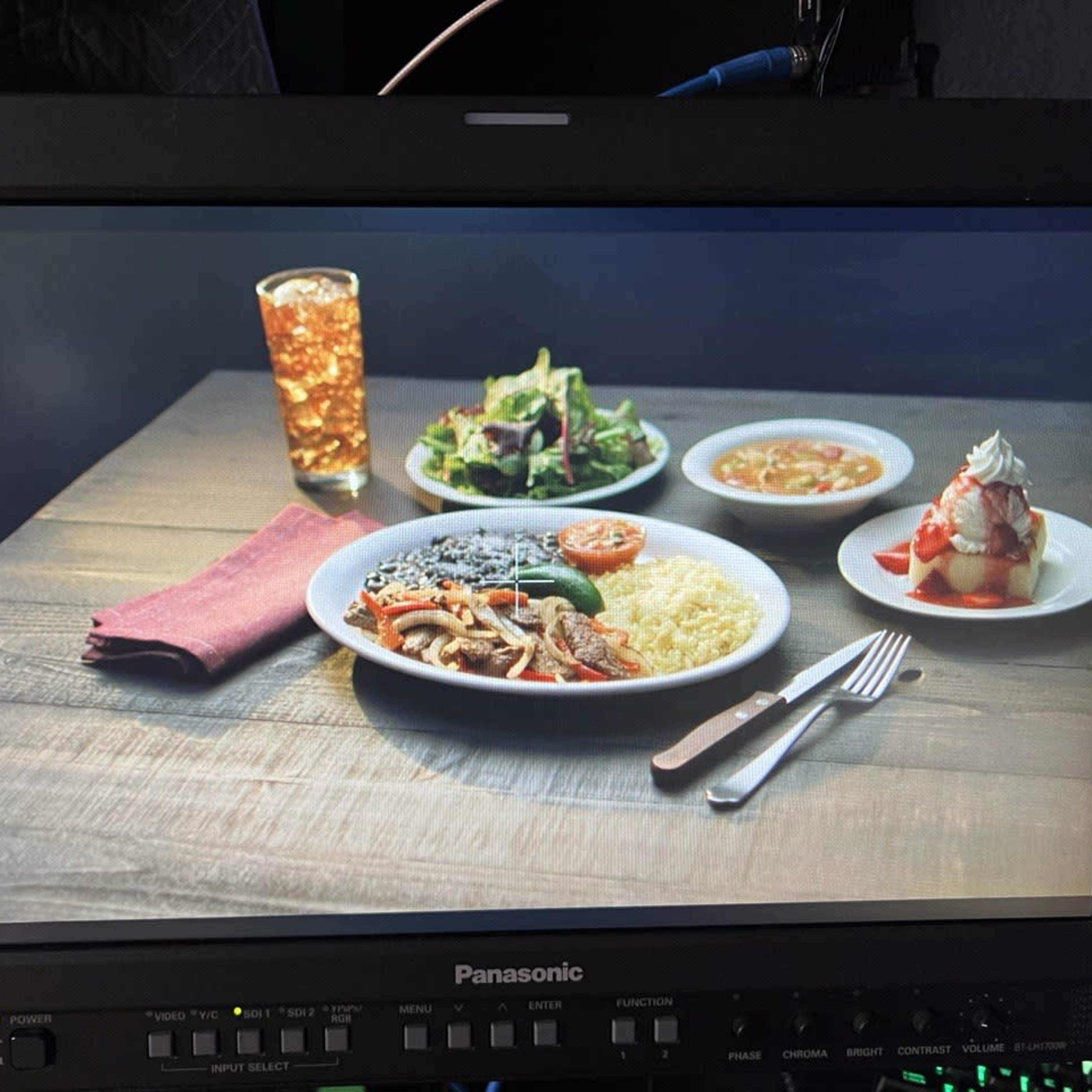 A television monitor displays a table setting with a plate of food, a salad, a dessert, and a glass of soda.