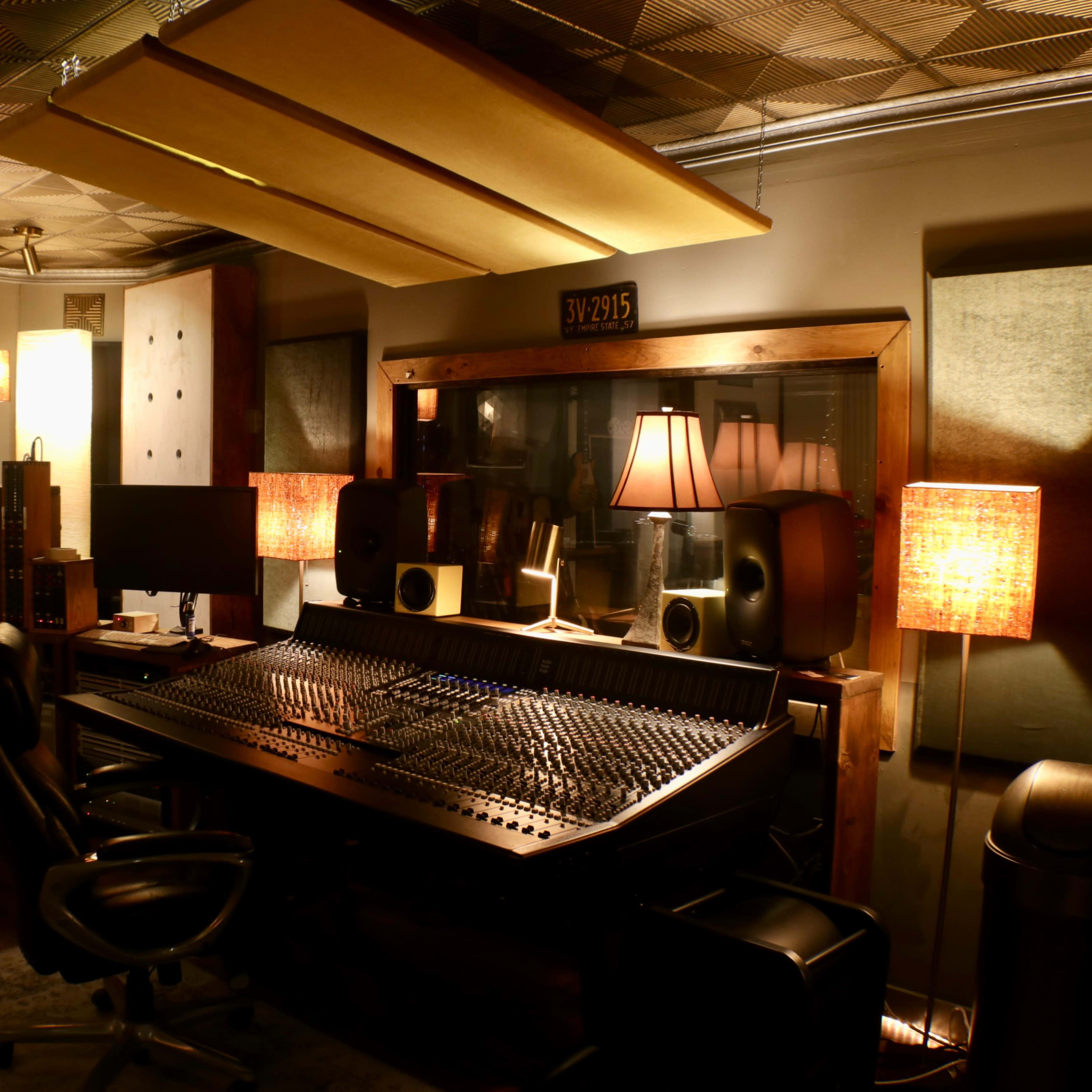 A dimly lit recording studio featuring a large mixing console, speakers, and ambient lamps.