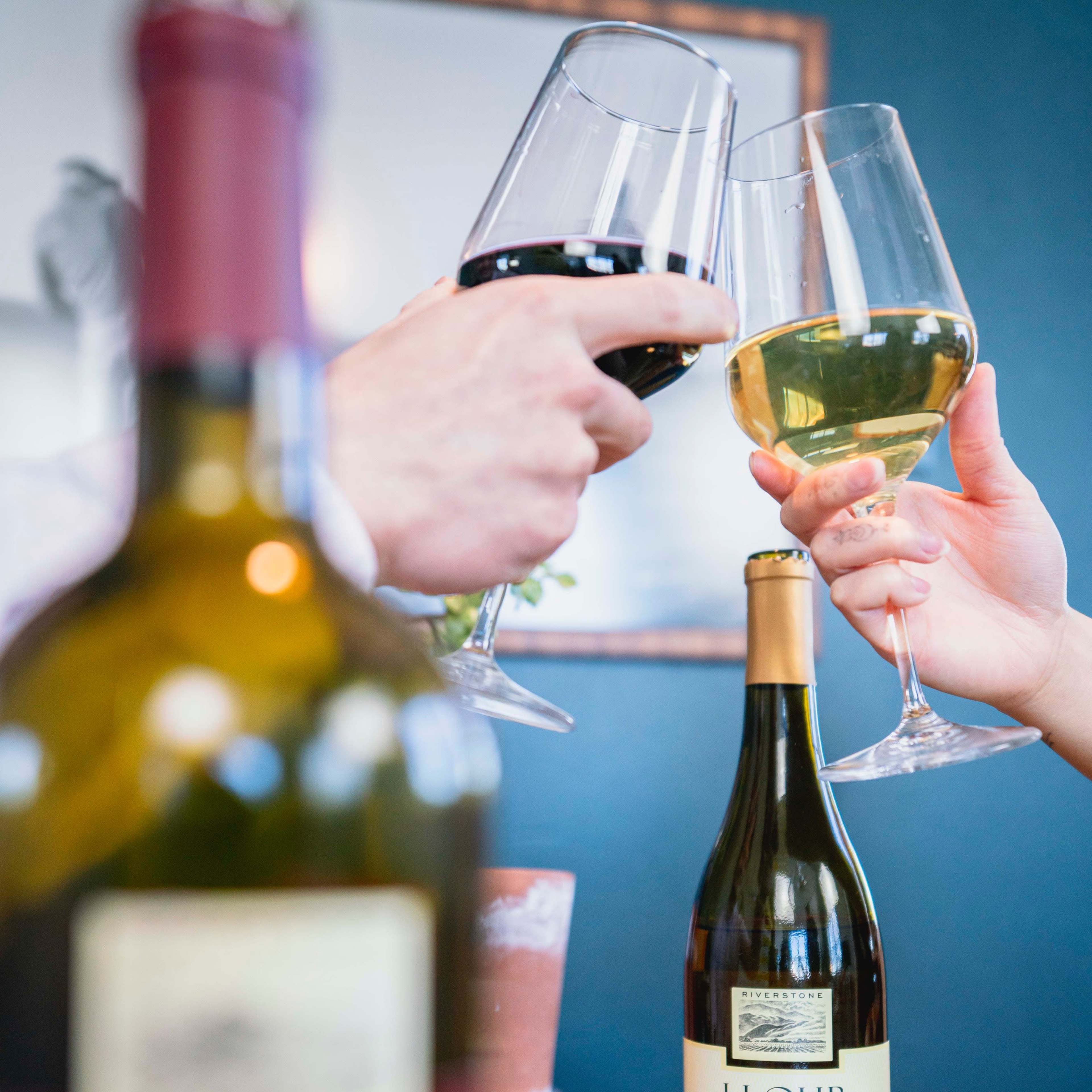 Two people clink glasses filled with red and white wine, with a J. Lohr wine bottle prominently displayed in the foreground.