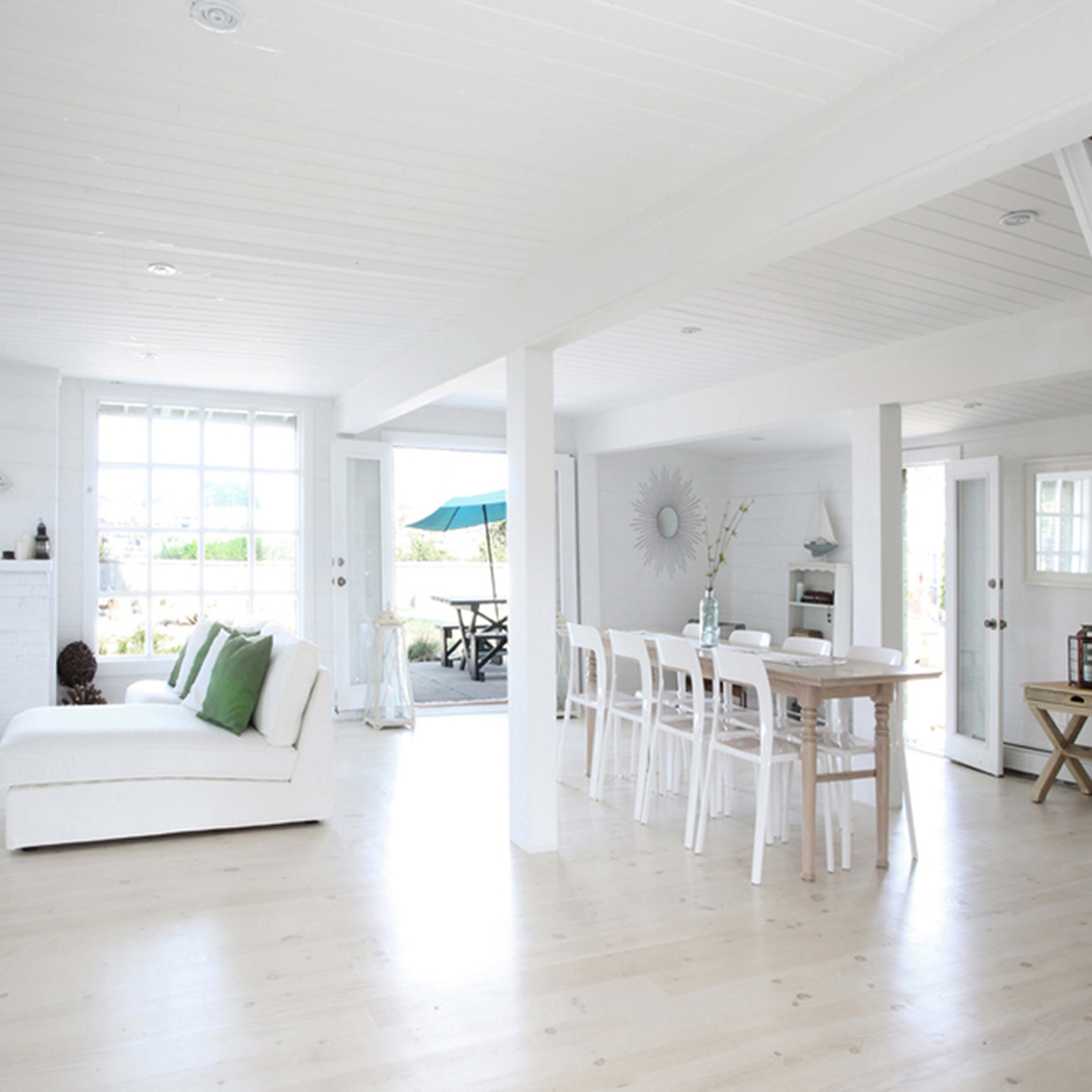 The image shows a bright, open-concept interior of a house with white walls, a fireplace, dining area, and a staircase leading to an upper level.