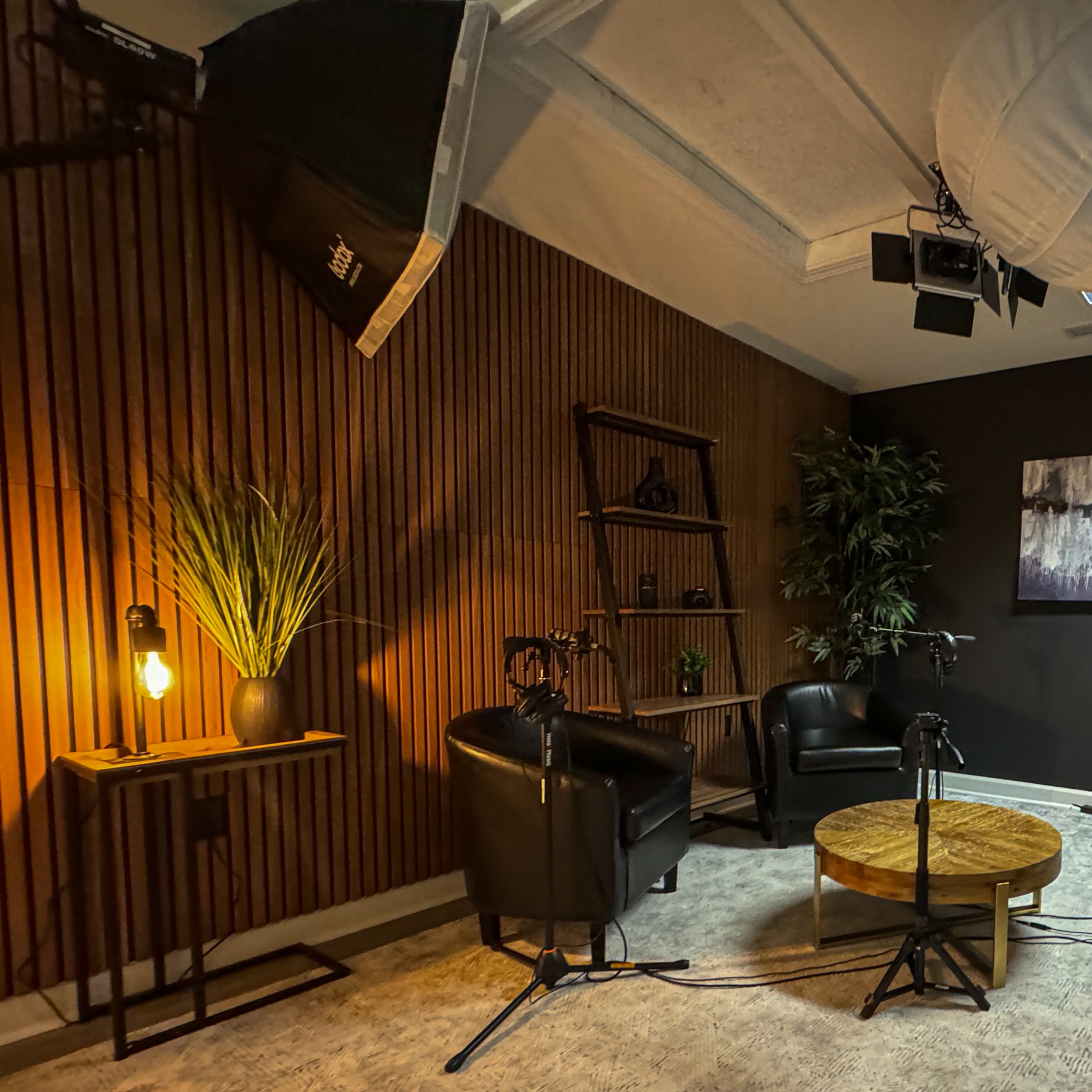 A small, modern recording studio with two chairs, a coffee table, and camera equipment set up in a stylishly decorated space.