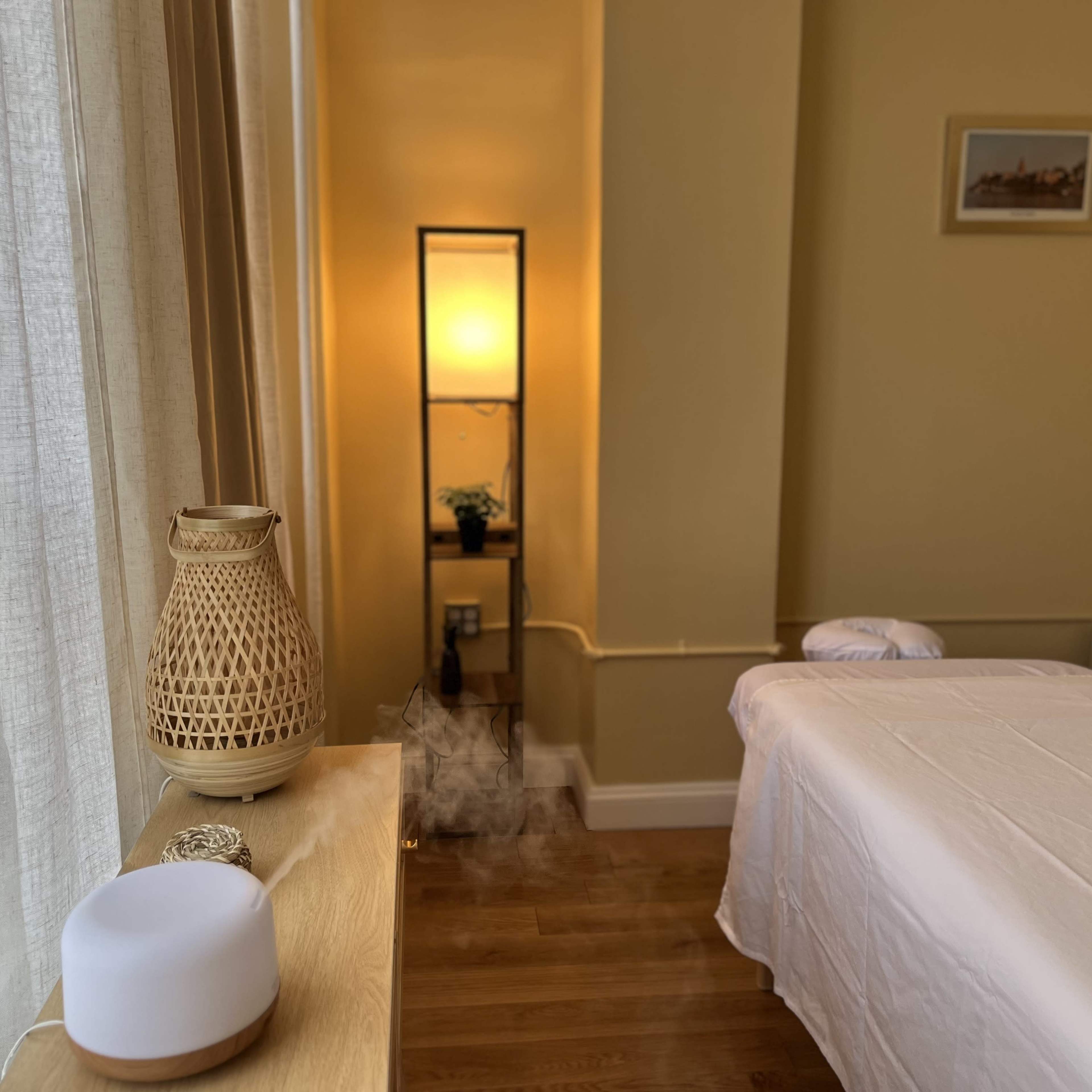 A serene room features a massage table, a glowing lamp, and a diffuser emitting a mist.