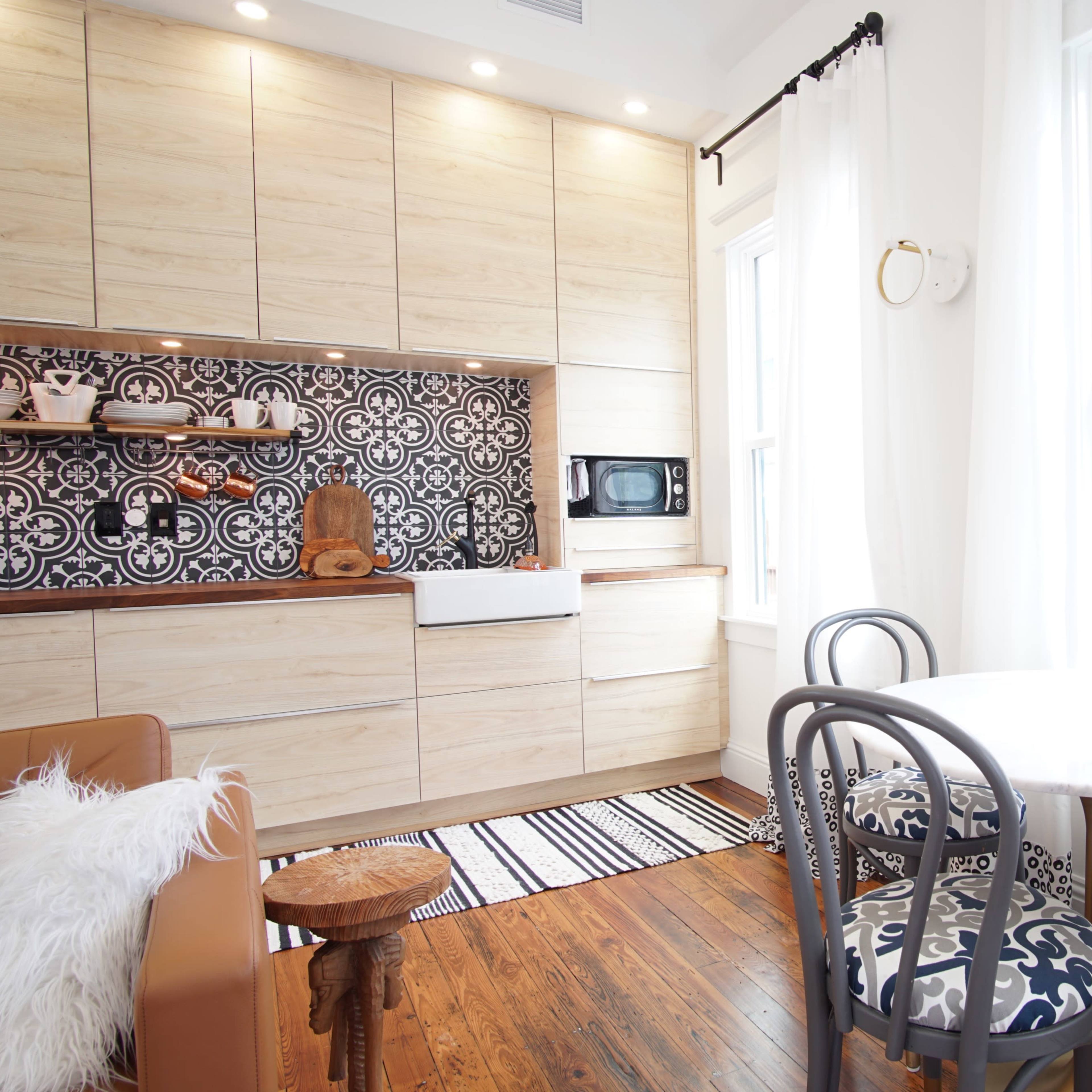 A modern kitchen features wooden cabinetry, a patterned backsplash, a small dining table, and a cozy seating area.