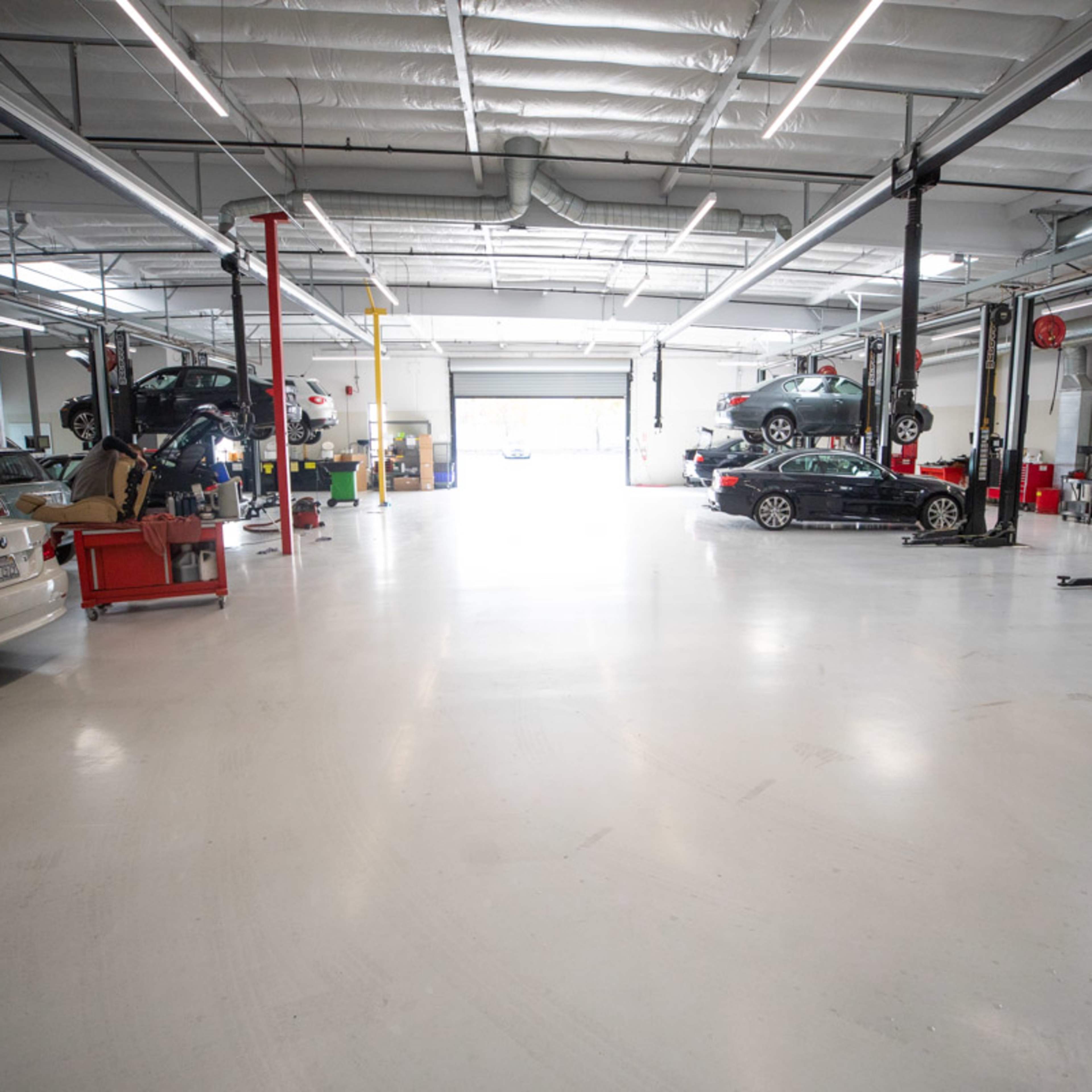 A spacious automotive workshop with multiple cars on lifts and tools organized on the floor.