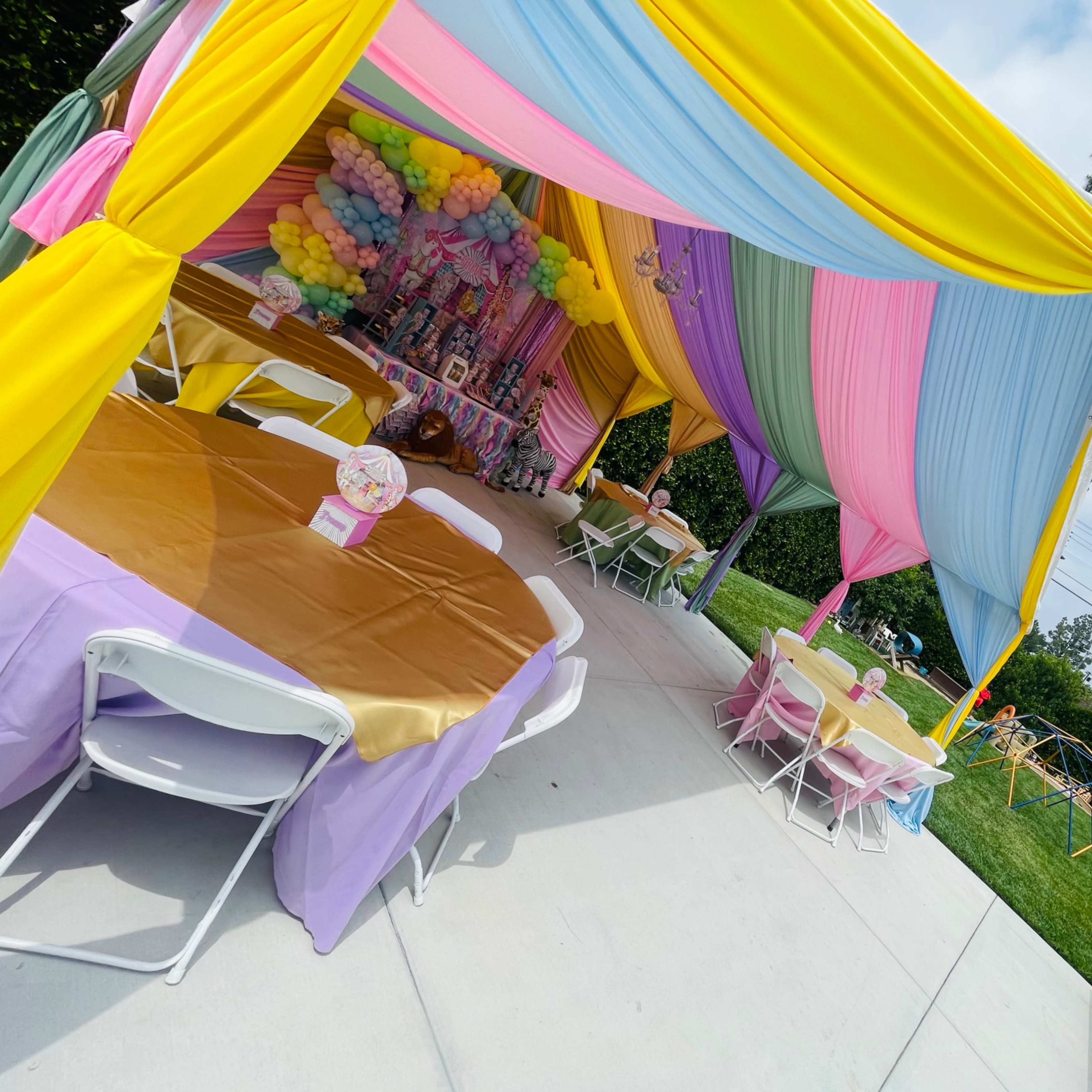 A colorful tent setup with decorated tables and balloons is arranged for an outdoor celebration.