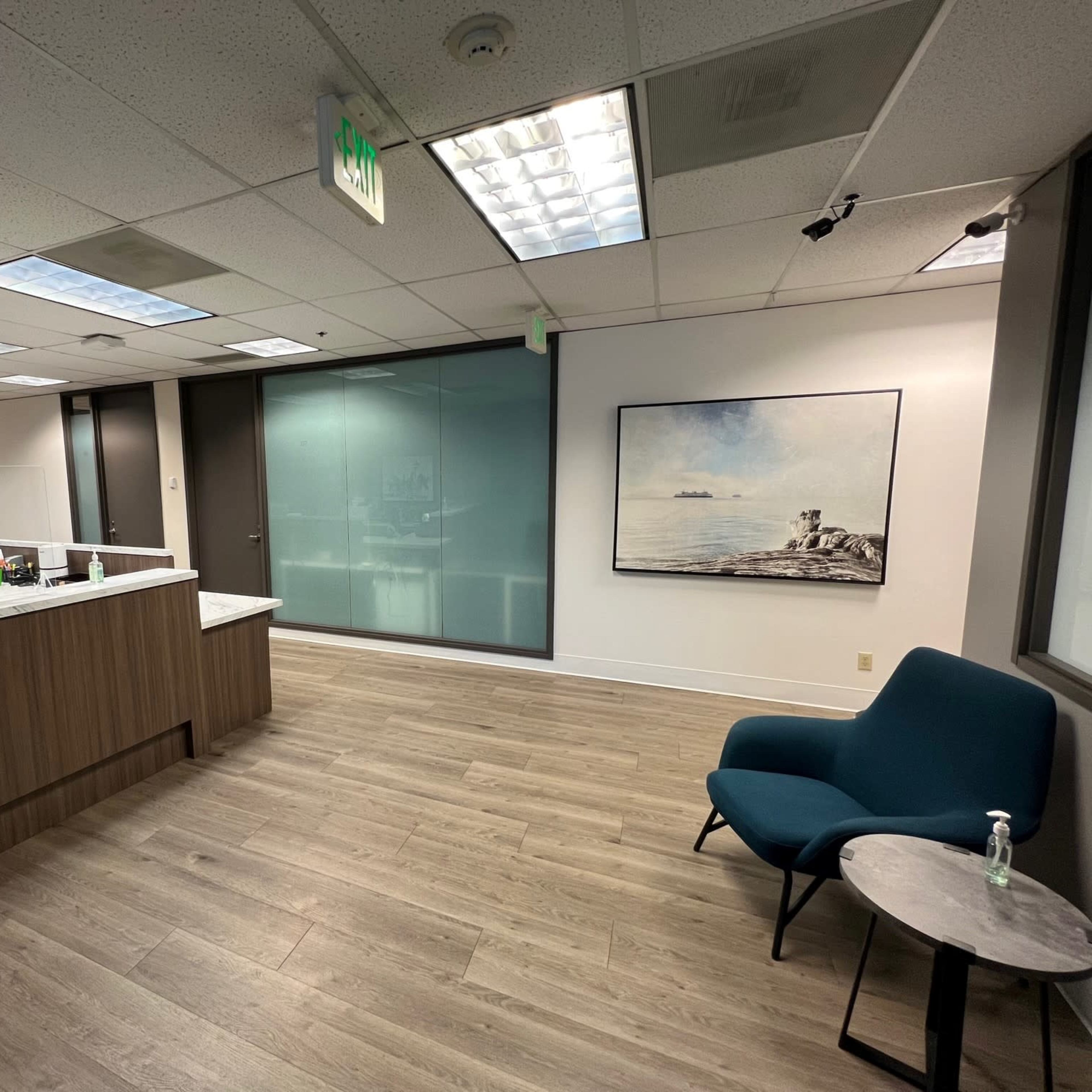 A modern office reception area with a desk, a blue chair, and a framed landscape painting on the wall.